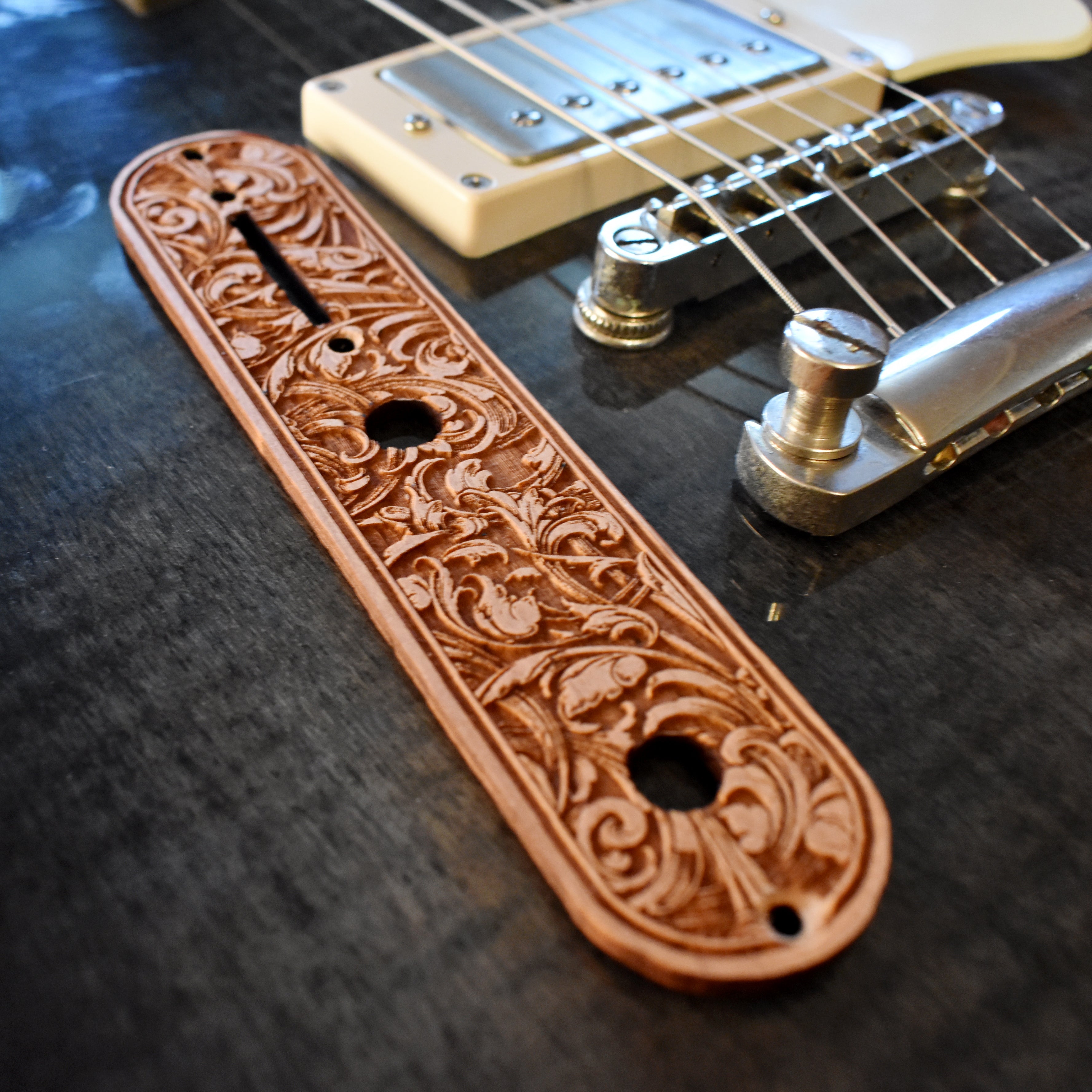 Laserβengraved wood trussβrod cover featuring elegant floral scrollwork design in light honeyβbrown finish