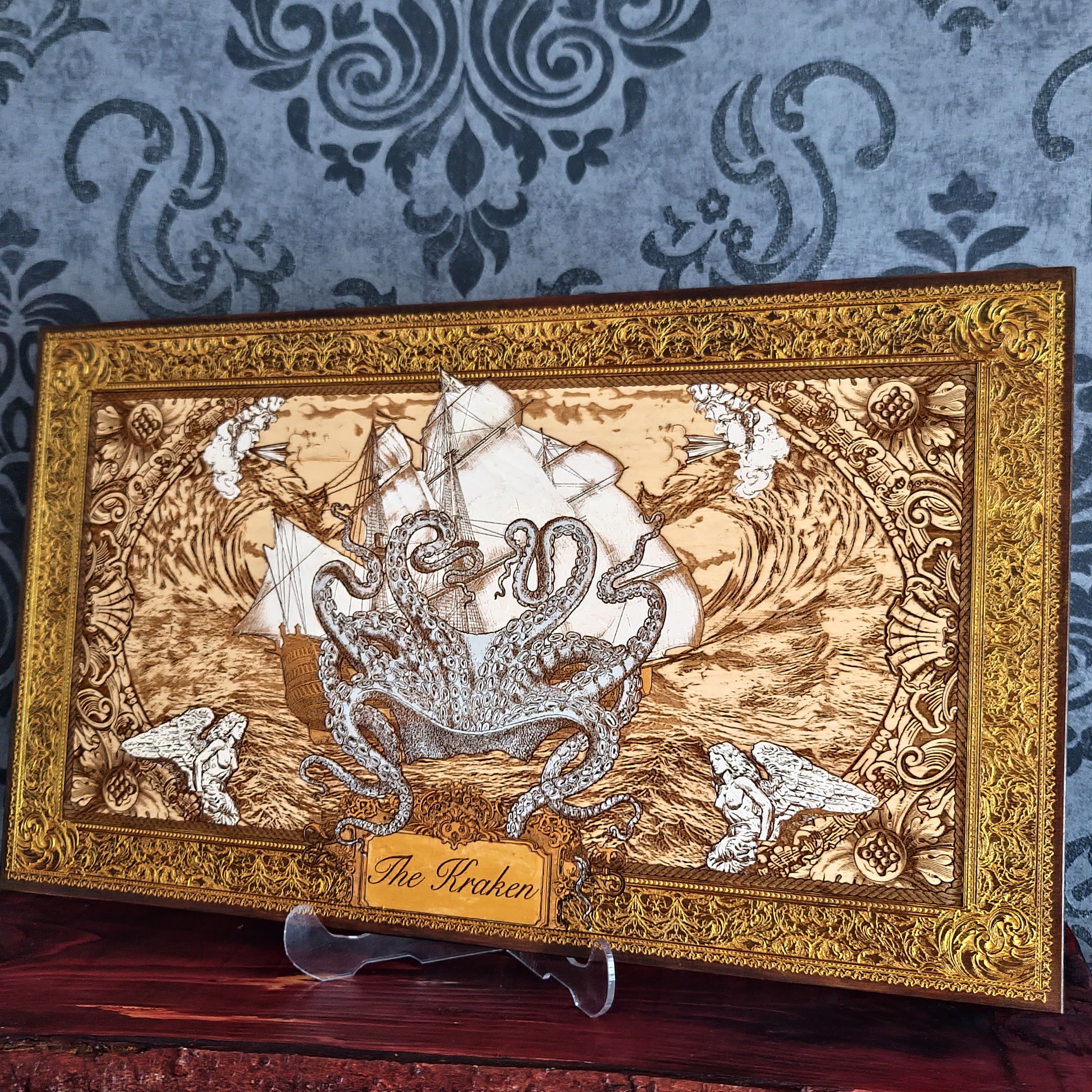 A framed decorative art piece featuring a detailed sepia-toned illustration of an octopus wrapped around a ship, with ornate gold-toned borders and a small plaque reading 'The Kraken.'