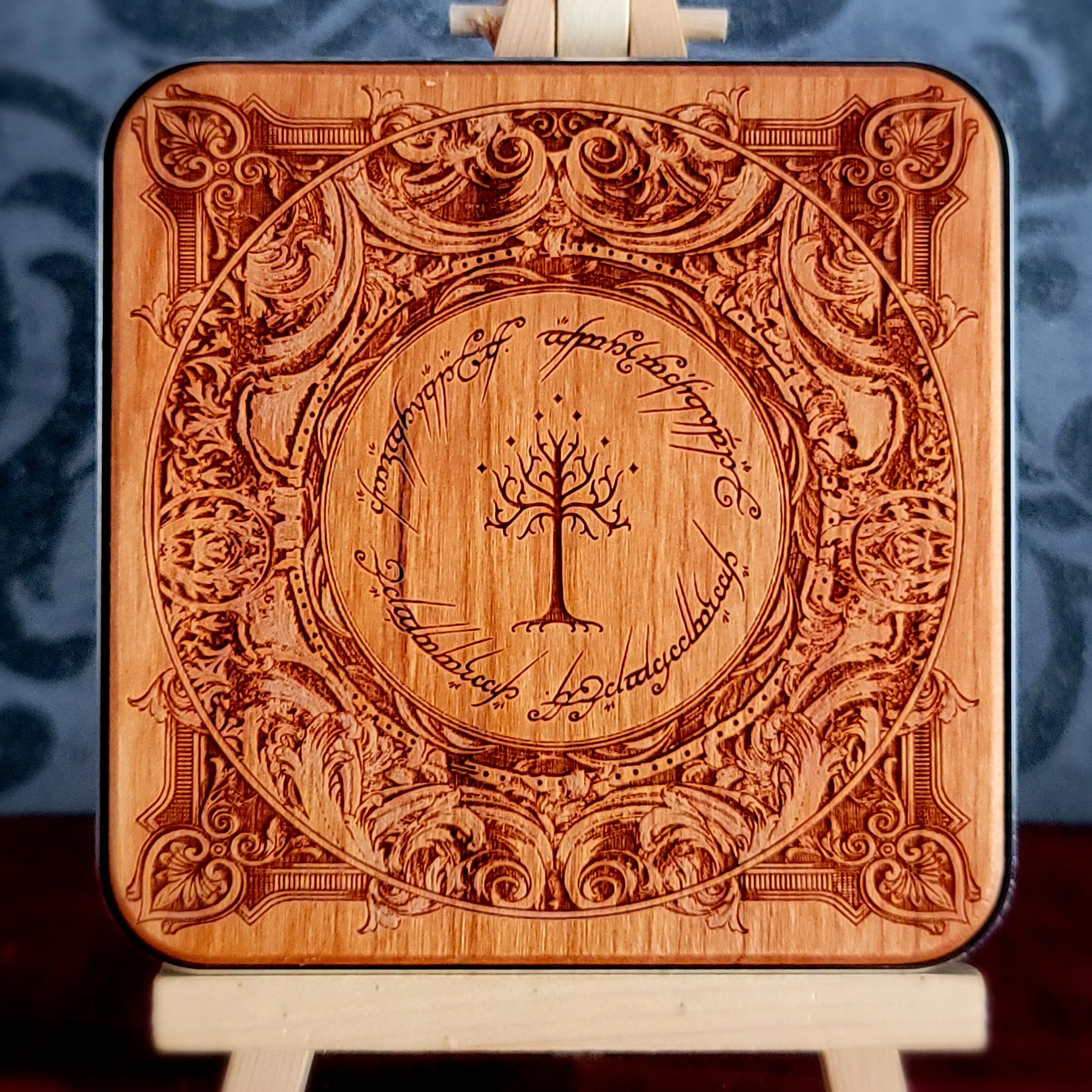 A square wooden wireless charger with rounded corners, featuring an intricate laser-engraved design inspired by 'The Lord of the Rings' with the Tree of Gondor in the center and the Ringwraith inscription around it.