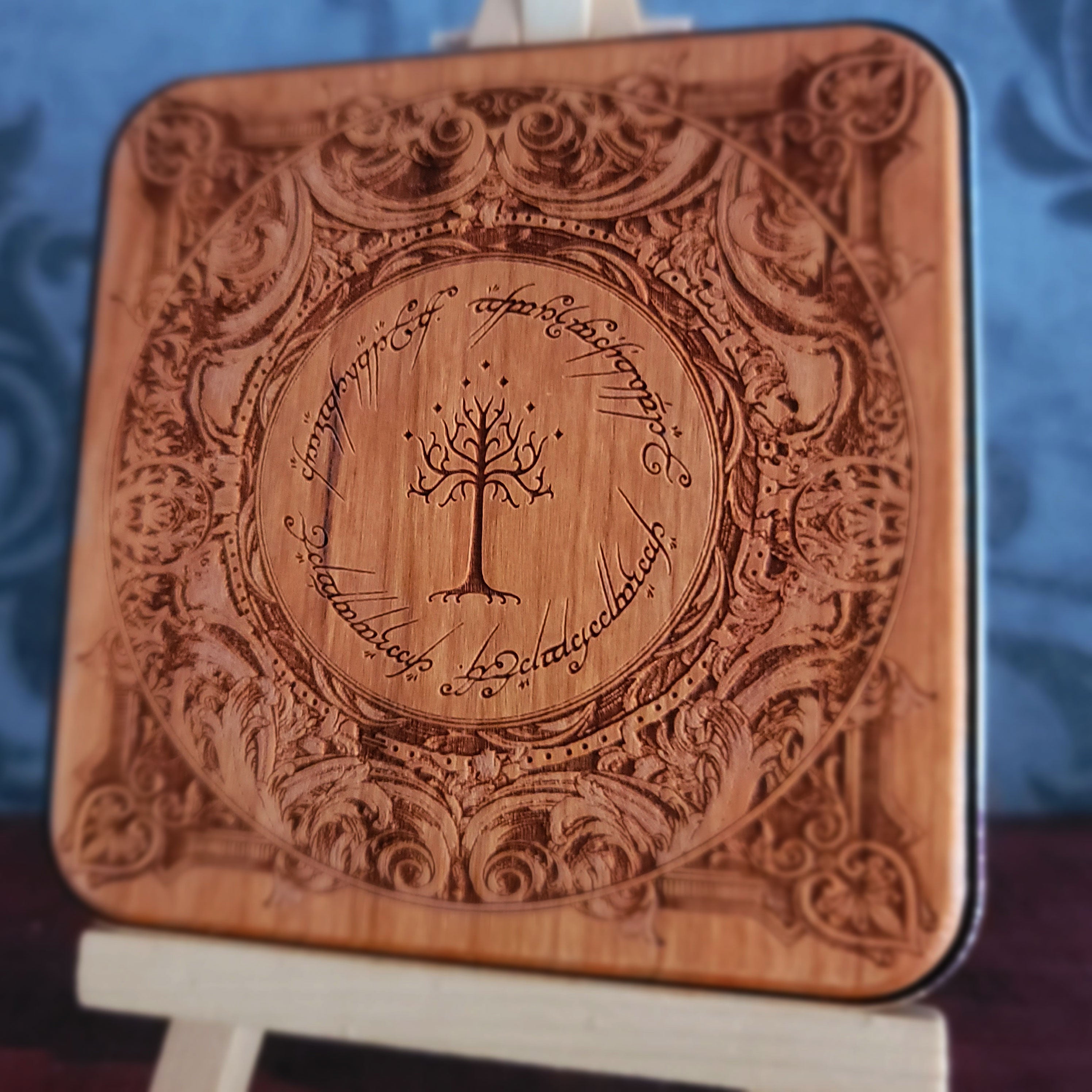 A square wooden wireless charger with rounded corners, featuring an intricate laser-engraved design inspired by 'The Lord of the Rings' with the Tree of Gondor in the center and the Ringwraith inscription around it.