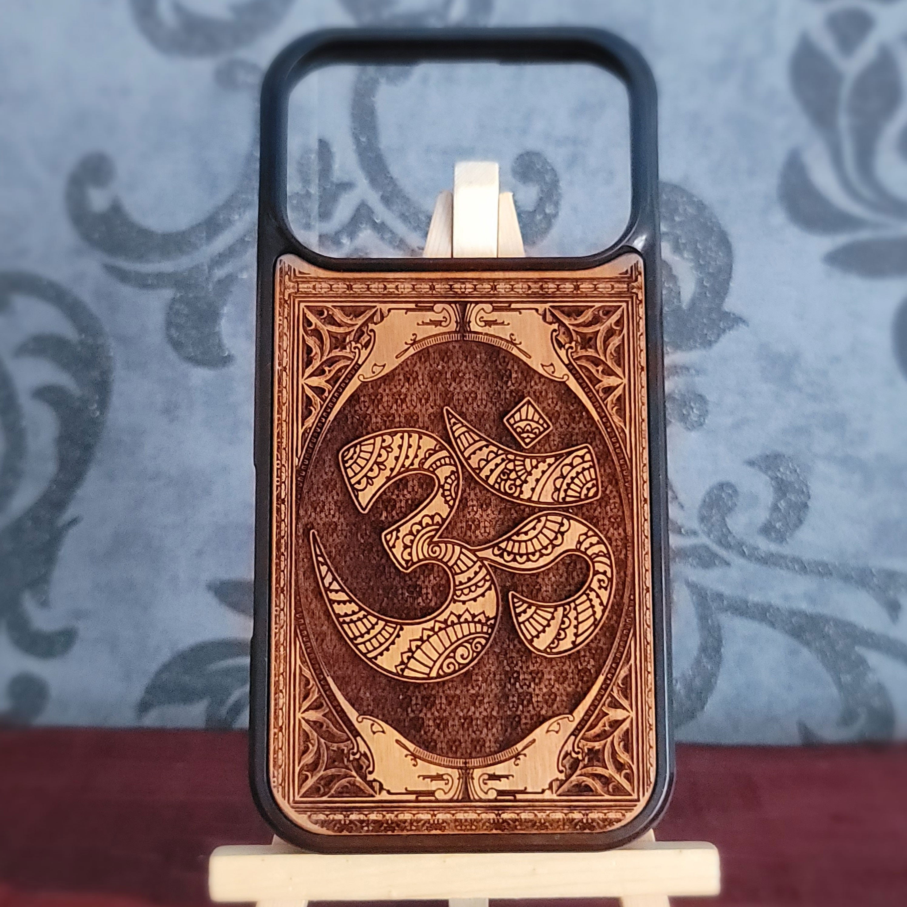 A wooden phone case with a laser-engraved Om symbol and ornate border details