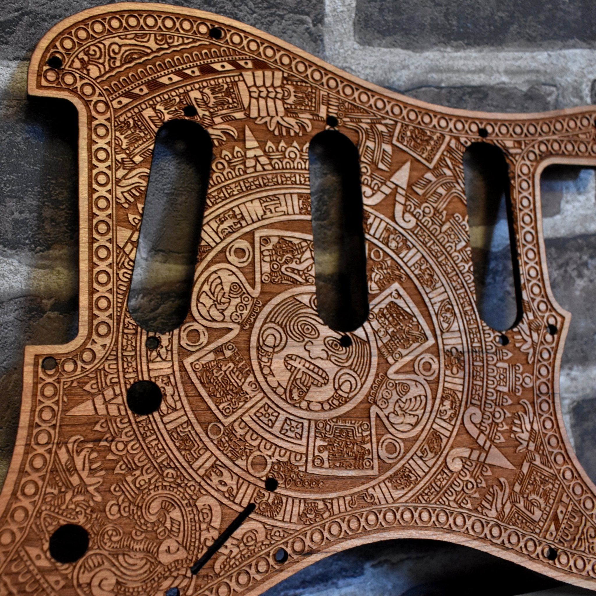 Close-up of laser-engraved cherry wood pickguard for a Fender Stratocaster guitar.