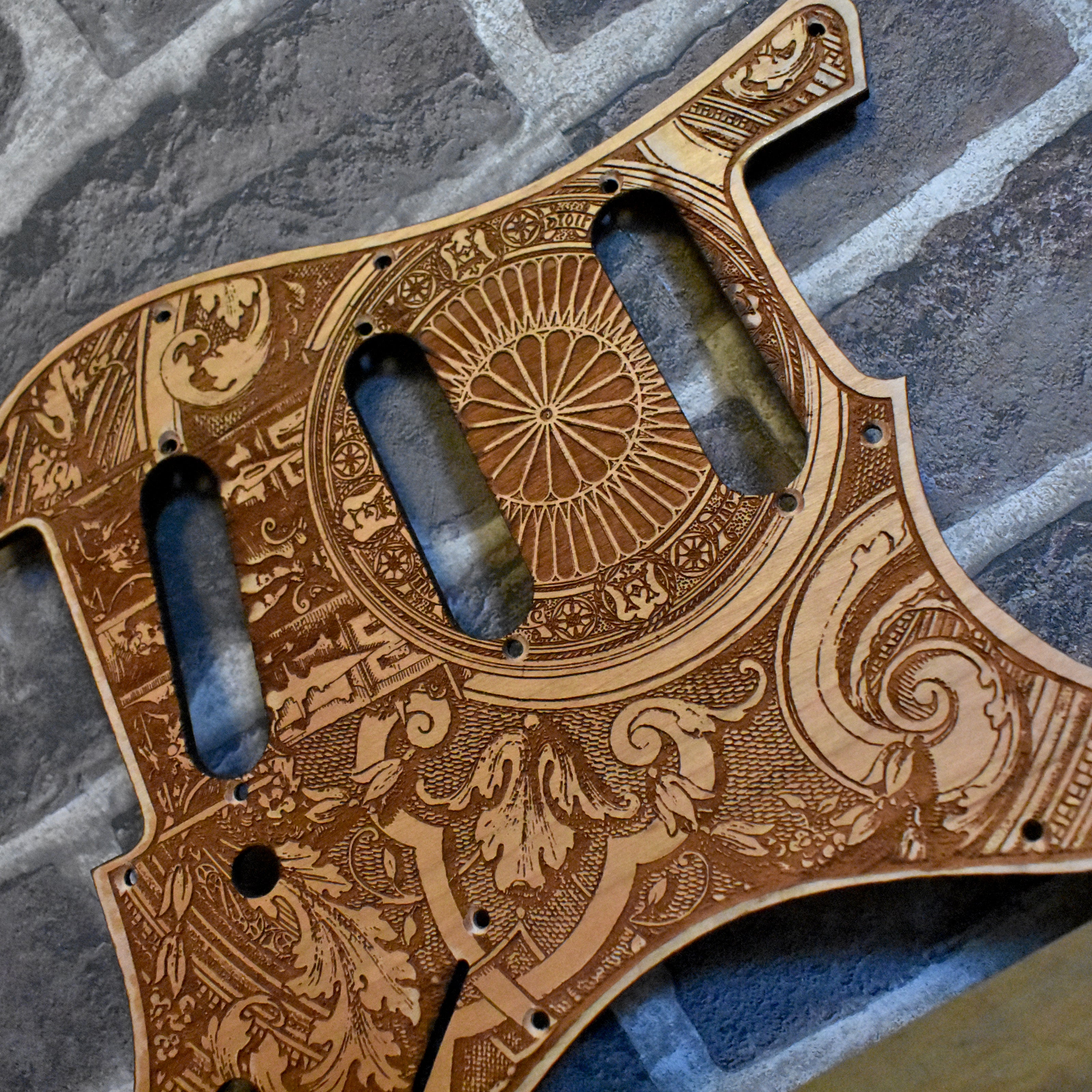 Close-up of laser-engraved cherry wood Fender Stratocaster pickguard with gothic artwork