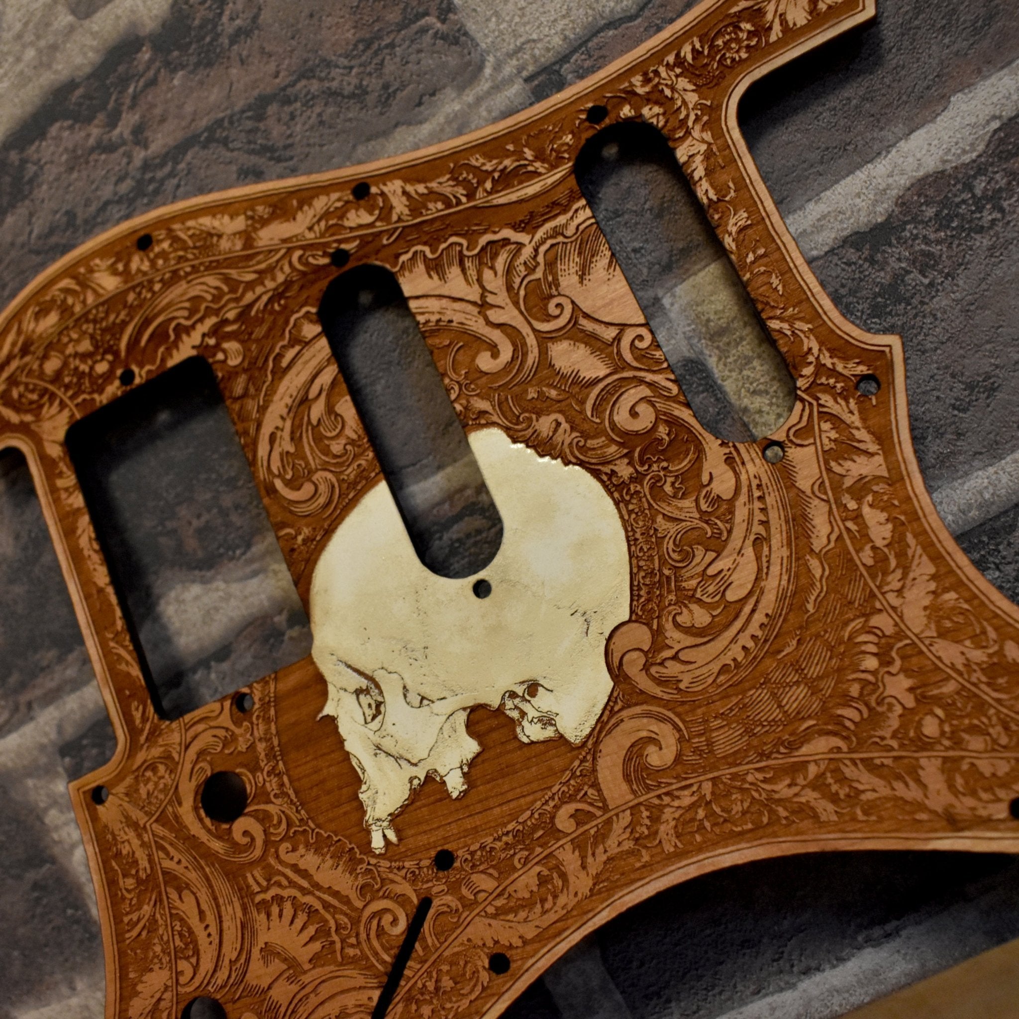 Close-up of laser-engraved human skull on cherry wood Fender Stratocaster pickguard.