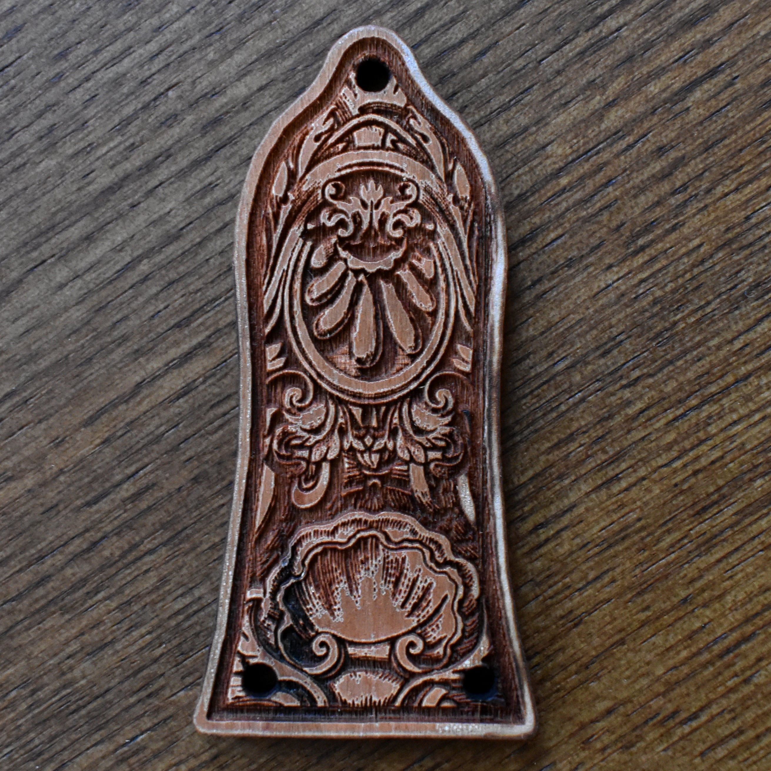 Laserβengraved wood trussβrod cover for an Epiphoneβstyle guitar. The wood has a warm mediumβbrown finish with visible grain. The design features a horizontal band of elegant floral scrollwork across the centre. Two small screw mounting holes are visible at the bottom edge.