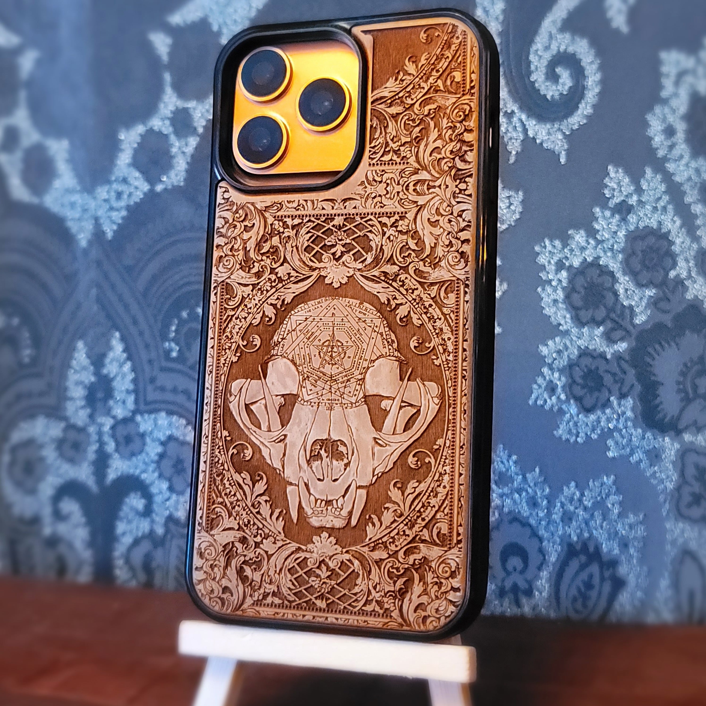 Deep laser engraved wooden phone case featuring a mystical cat skull design with witchy dark art details on natural wood for iPhone and Samsung Galaxy models.