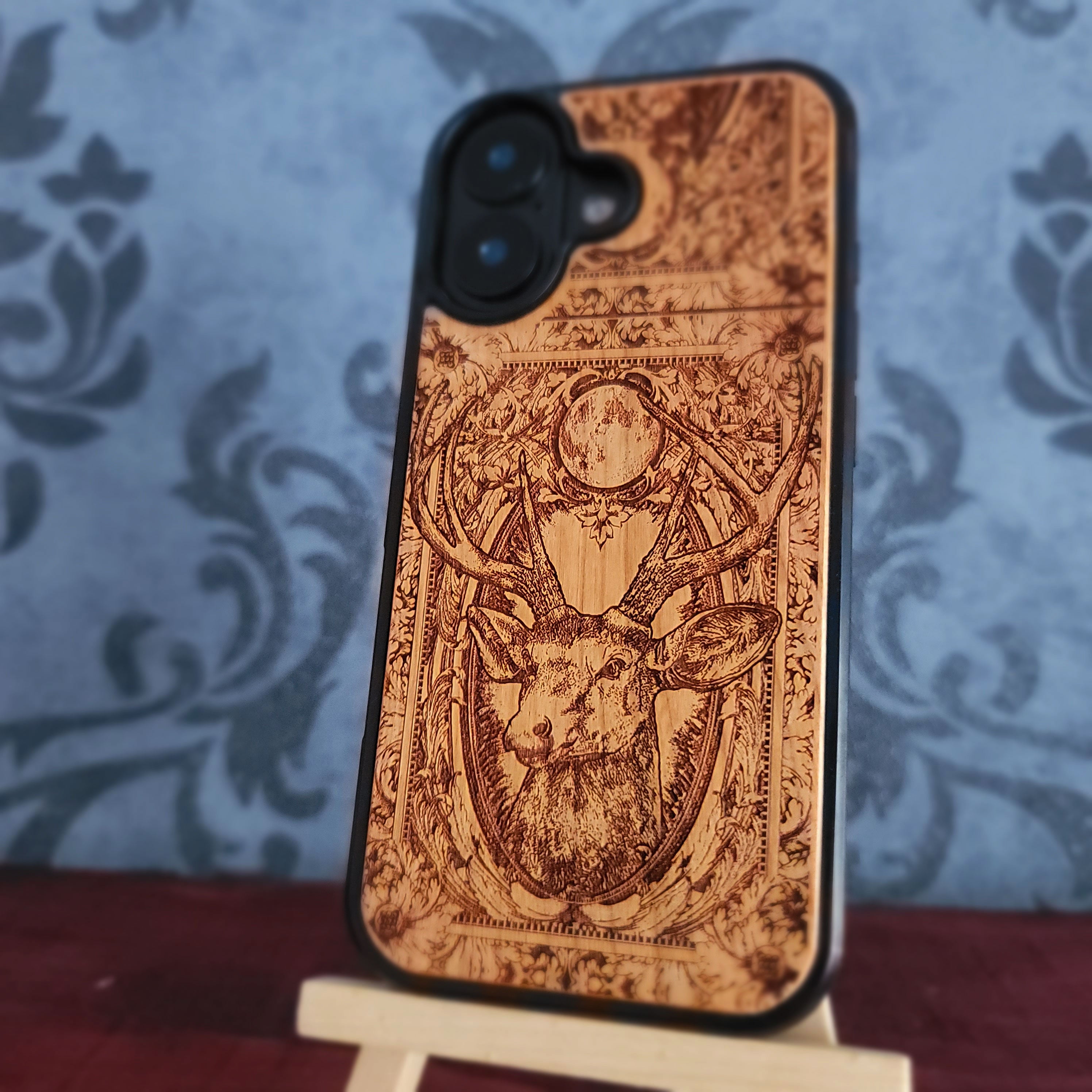 A smartphone case with a laser-engraved deer head and ornate border design,