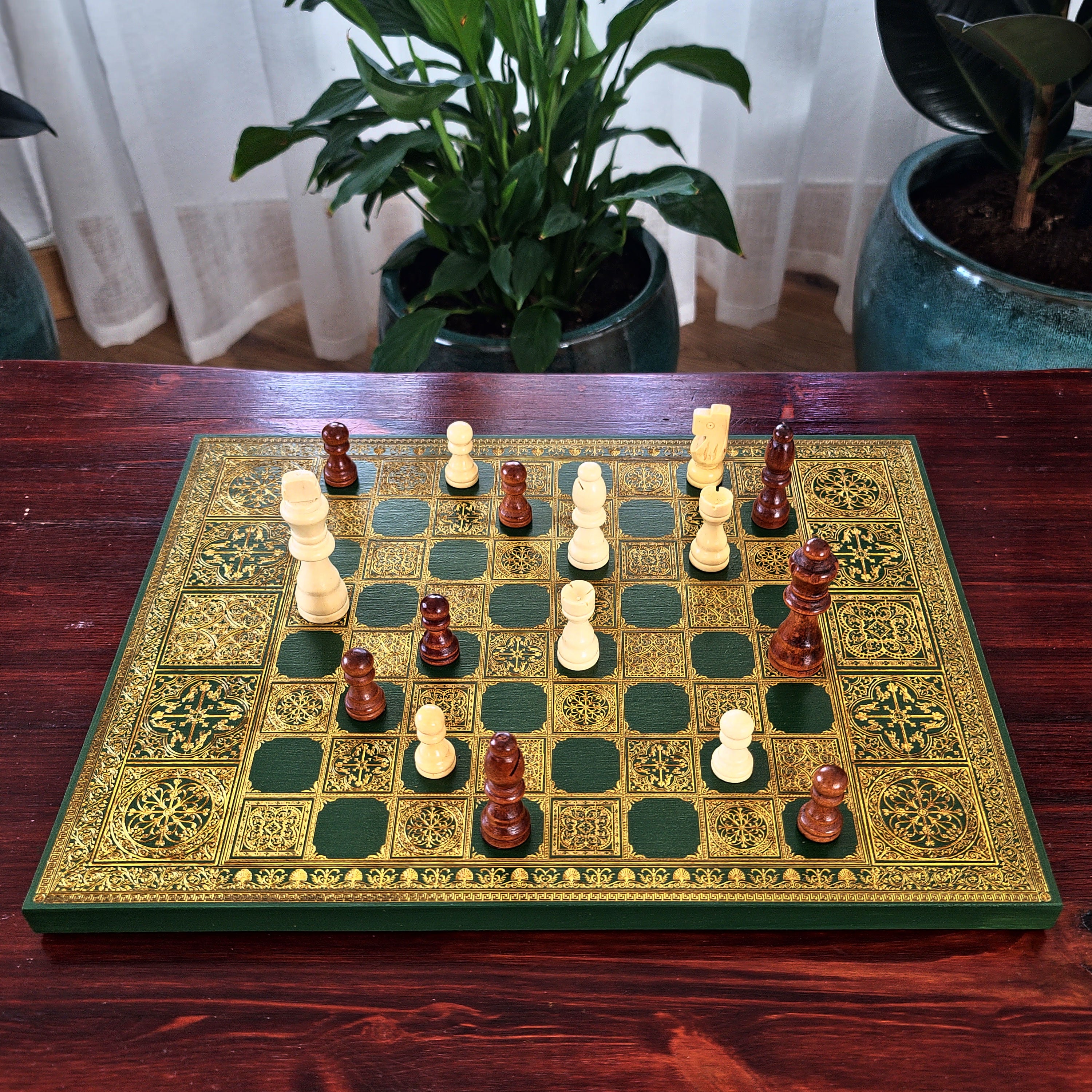 An ornate wooden chess set with a green and gold patterned board and dark red and cream chess pieces