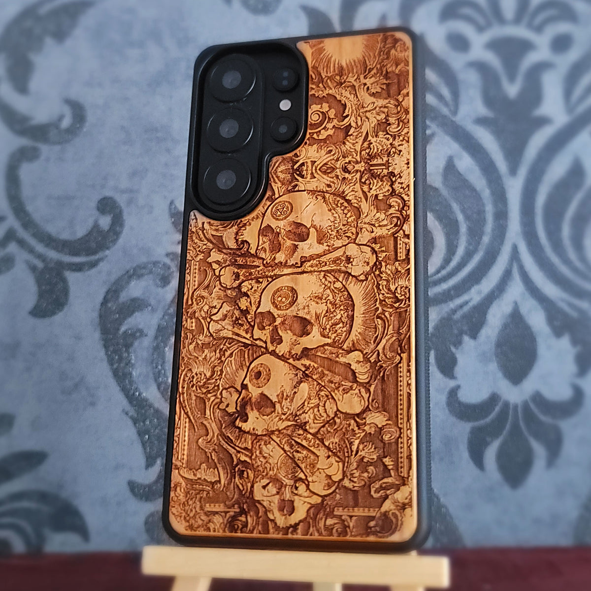 Gothic wooden phone case with pile of skulls and intricate macabre artwork