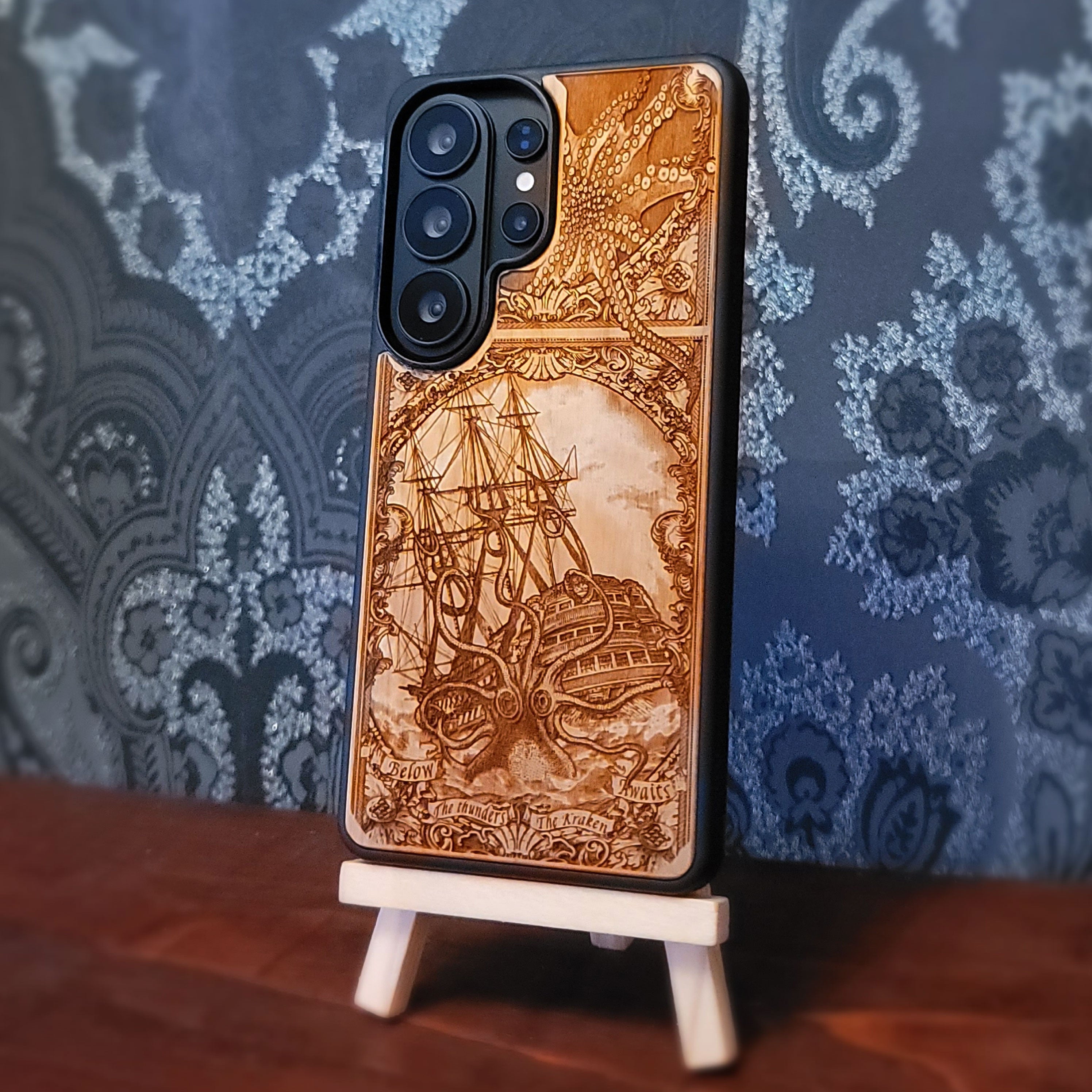 Laser engraved and hand painted wooden phone case featuring a giant Kraken sea monster attacking a ship for iPhone and Samsung Galaxy models.