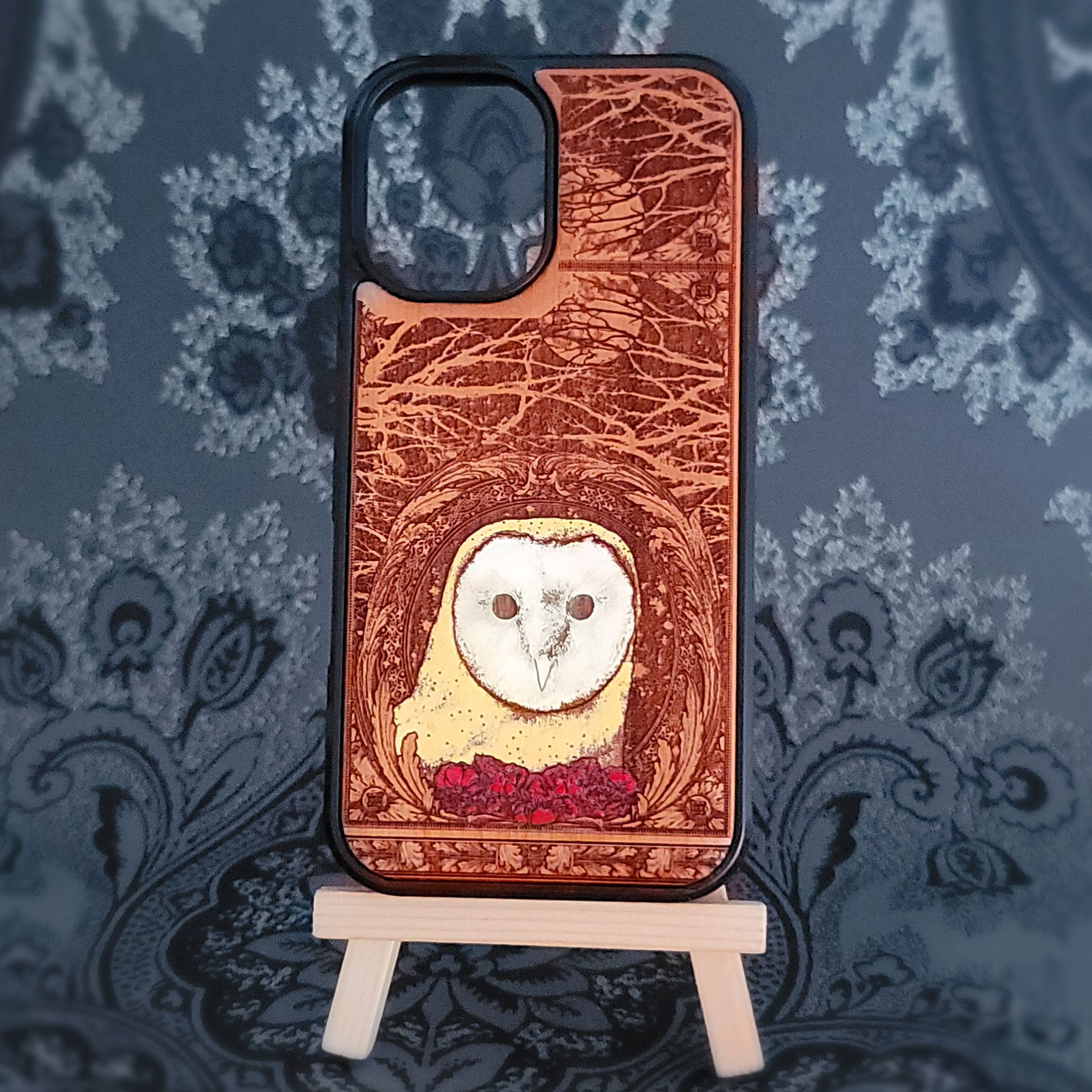 Phone case with owl design on a decorative stand against a patterned background