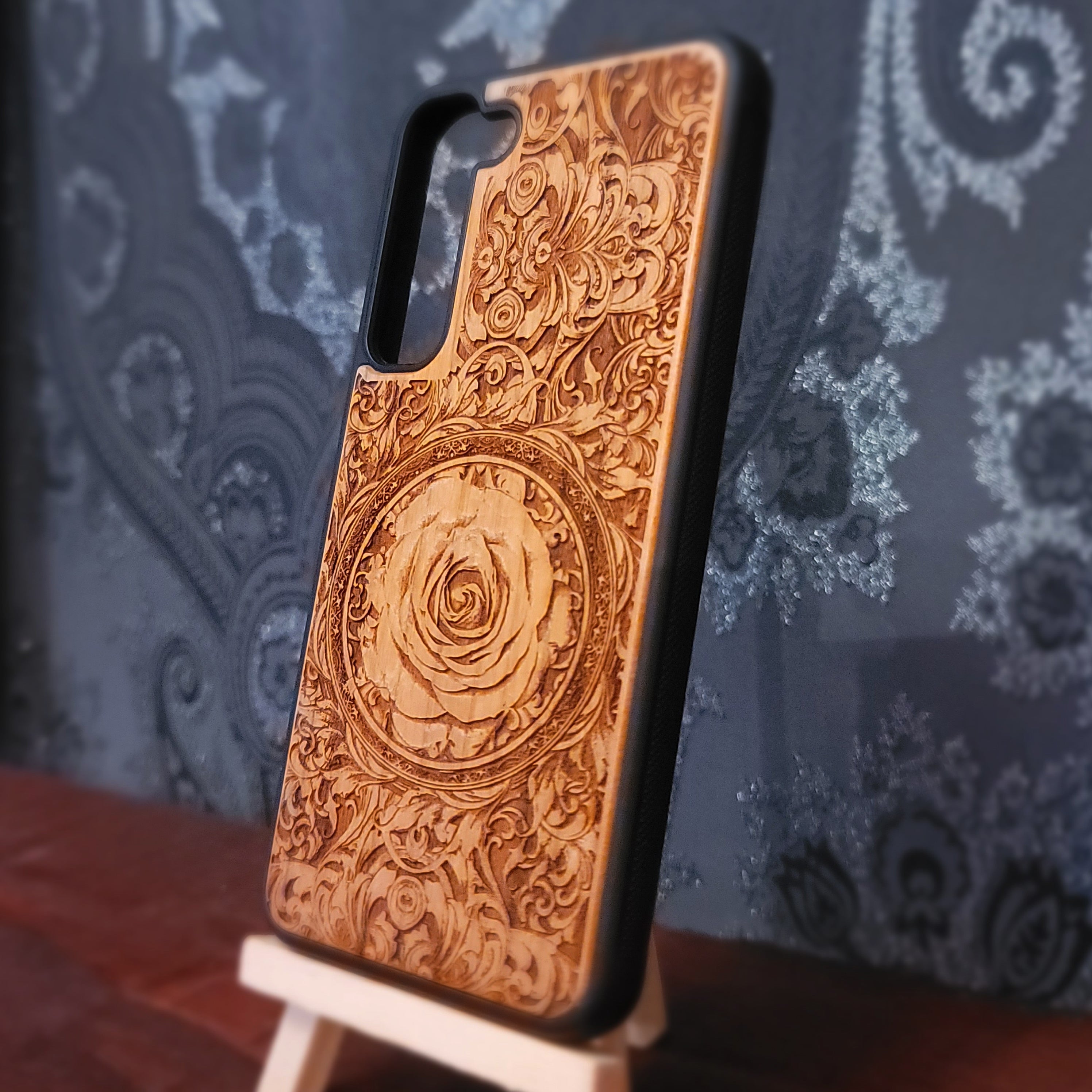 Deep laser engraved wooden phone case featuring an intricate floral design with a large detailed rose on natural wood for iPhone and Samsung Galaxy models.