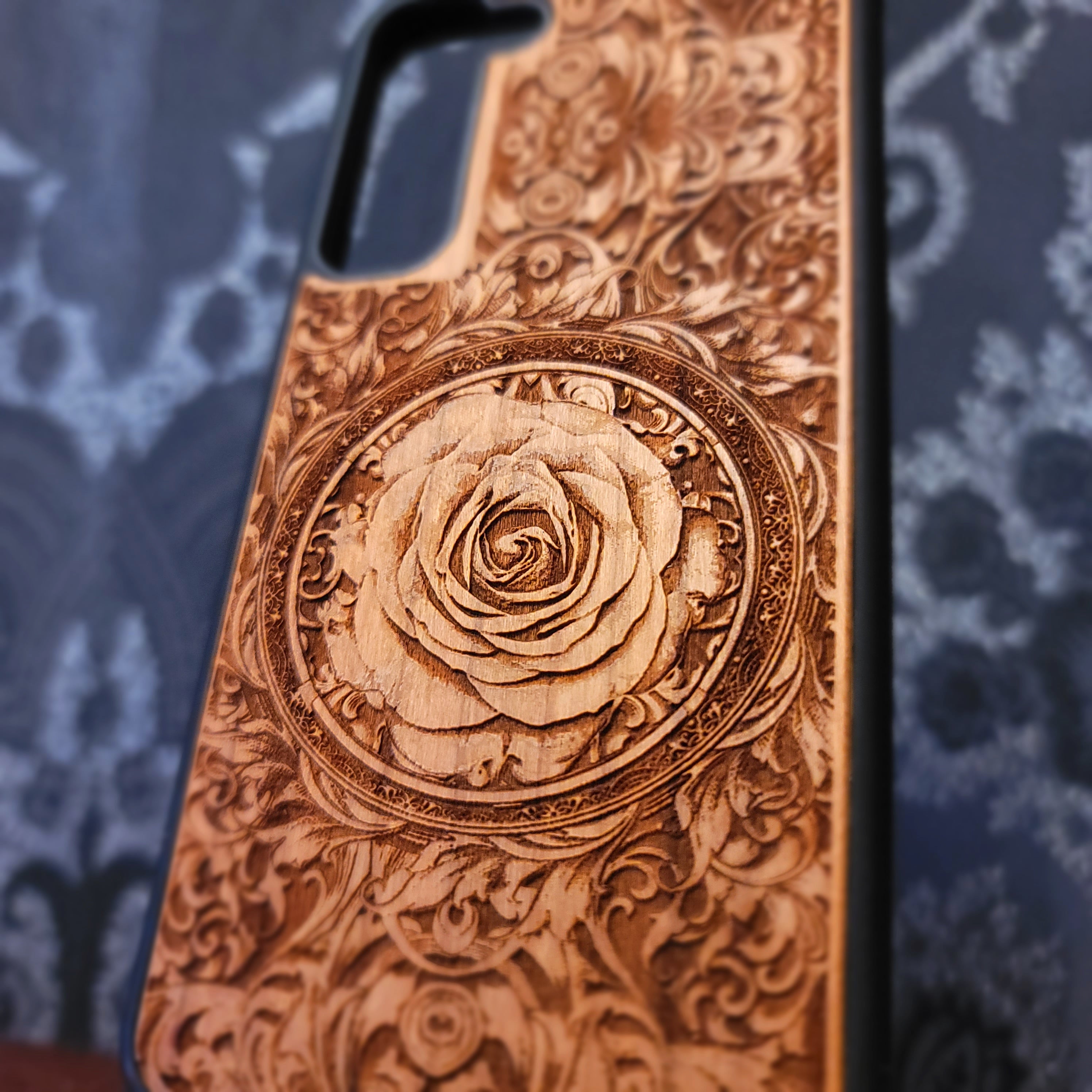 Deep laser engraved wooden phone case featuring an intricate floral design with a large detailed rose on natural wood for iPhone and Samsung Galaxy models.