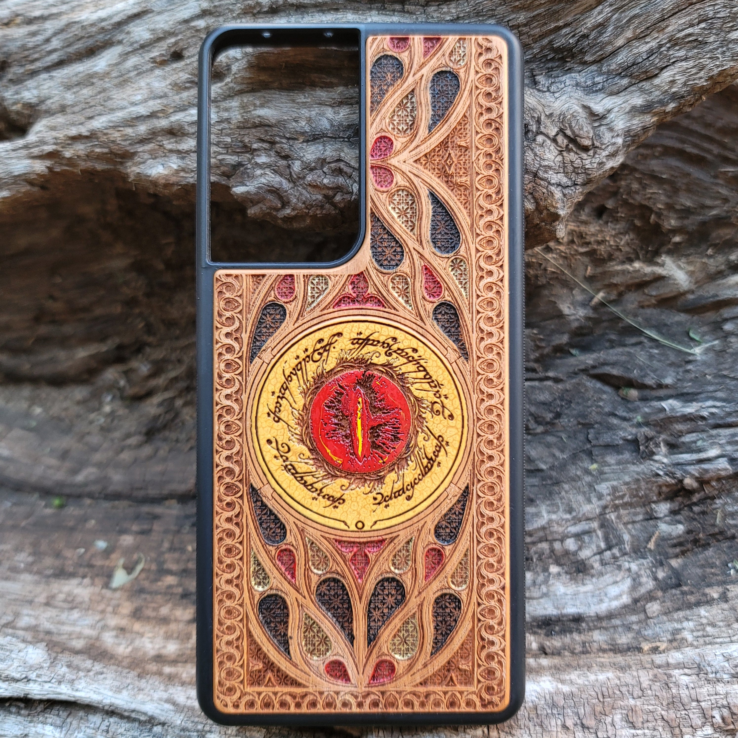 "Hand-painted wood phone case featuring the Eye of Sauron surrounded by intricate Elvish script and vibrant colored patterns. This laser-engraved and detailed design offers a unique blend of artistry and durability. Compatible with iPhone , 15, 14, 13, 12, 11, Pro Max, Mini, and Samsung Galaxy S, S24, S23, S22, S21, S20 Ultra, Plus, Note 20. Perfect for Lord of the Rings fans seeking a bold and protective accessory