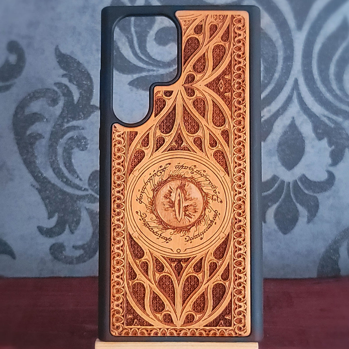 A wooden phone case with an intricate laser-engraved design inspired by The Lord of the Rings, featuring the Eye of Sauron in the center a