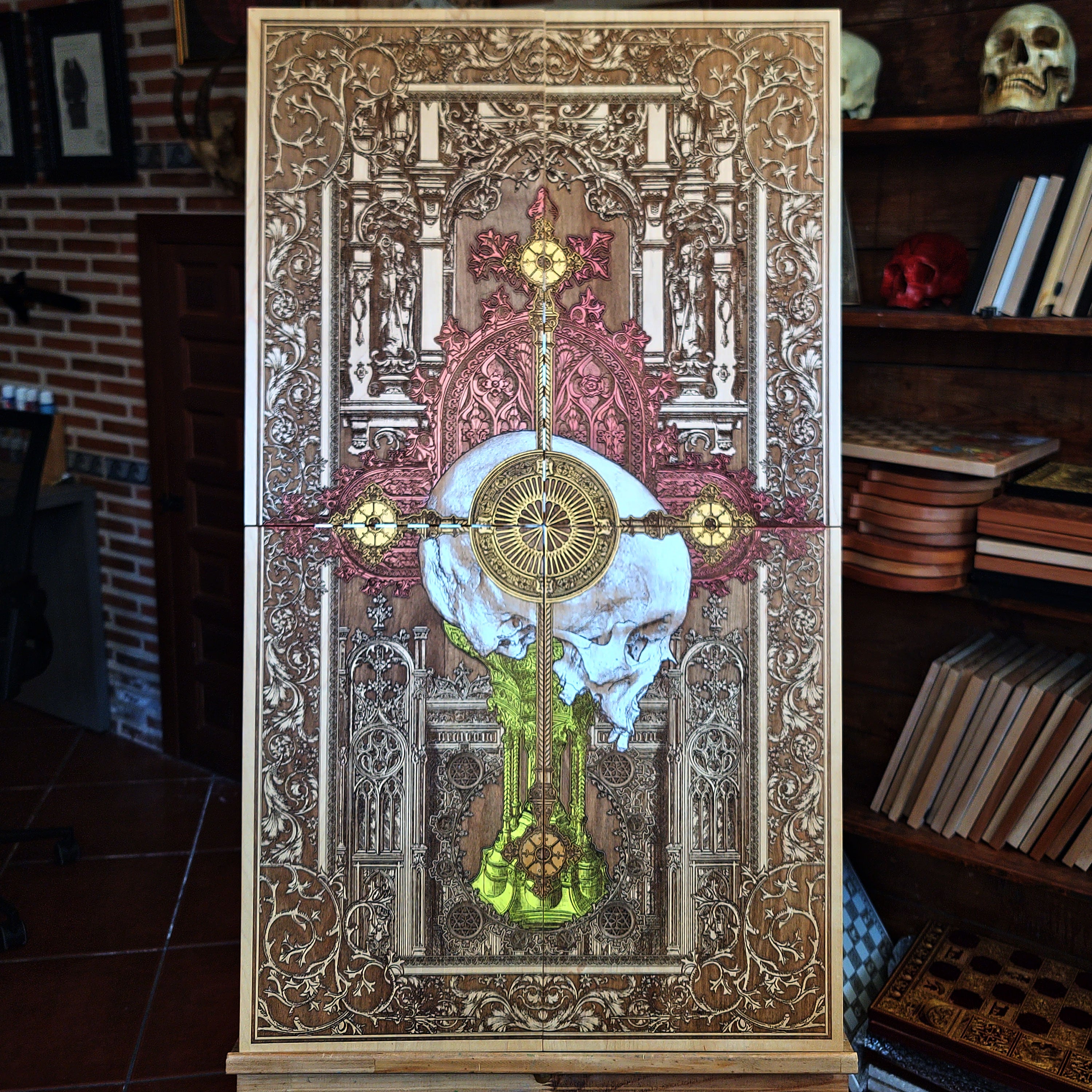 A detailed wooden artwork featuring a skull at the center, overlaid with a cross and intricate gothic architectural elements. The artwork is primarily brown with accents of gold, red, and yellow.