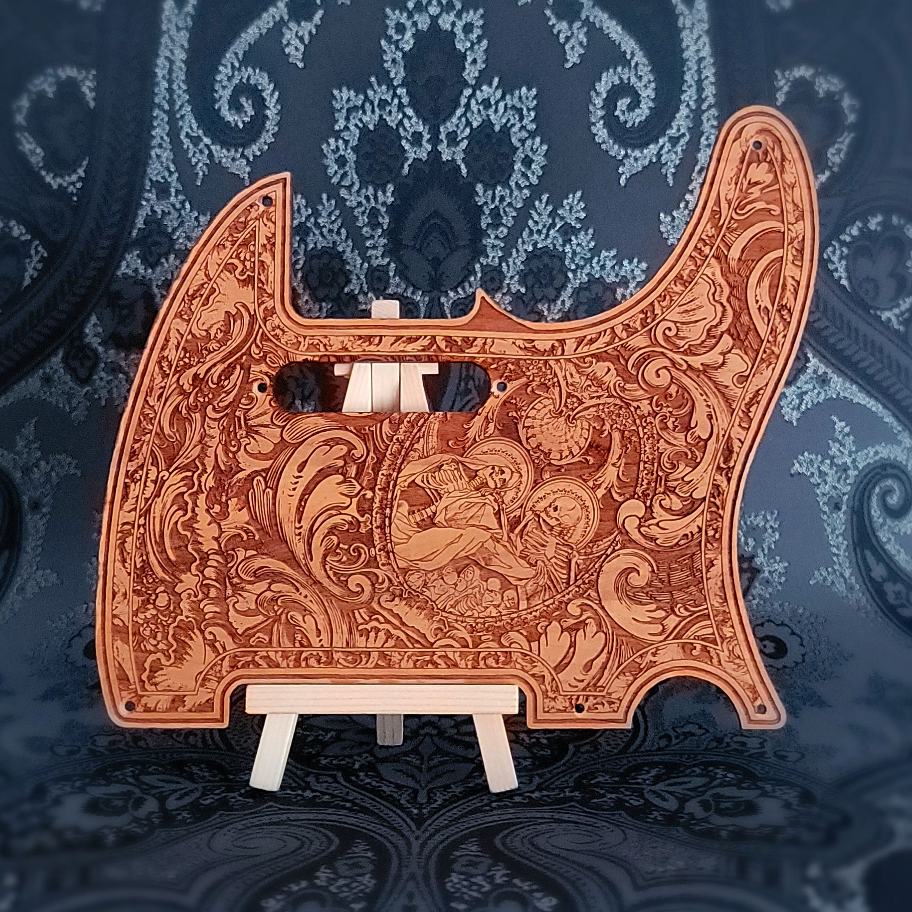 A wooden guitar pickguard with an intricate laser-etched design featuring a skeletal figure and floral patterns.
