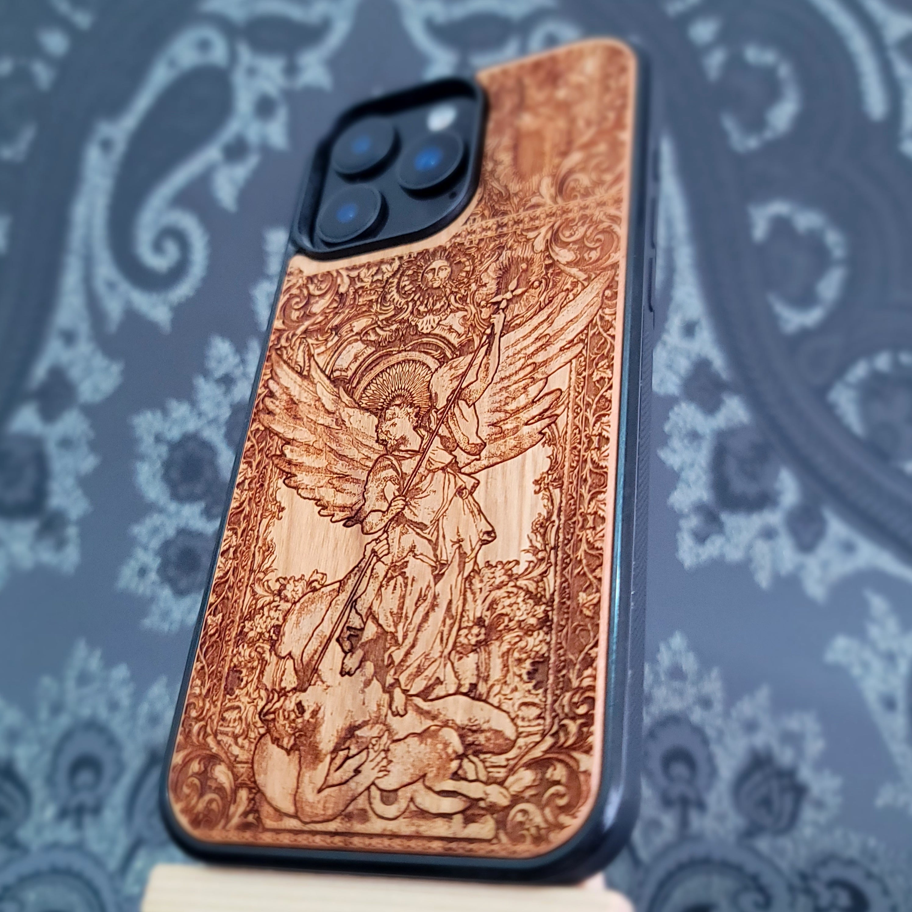 Deep laser engraved wooden phone case featuring Saint Michael Archangel fighting a demon with detailed religious artwork on natural wood for iPhone and Samsung Galaxy models.