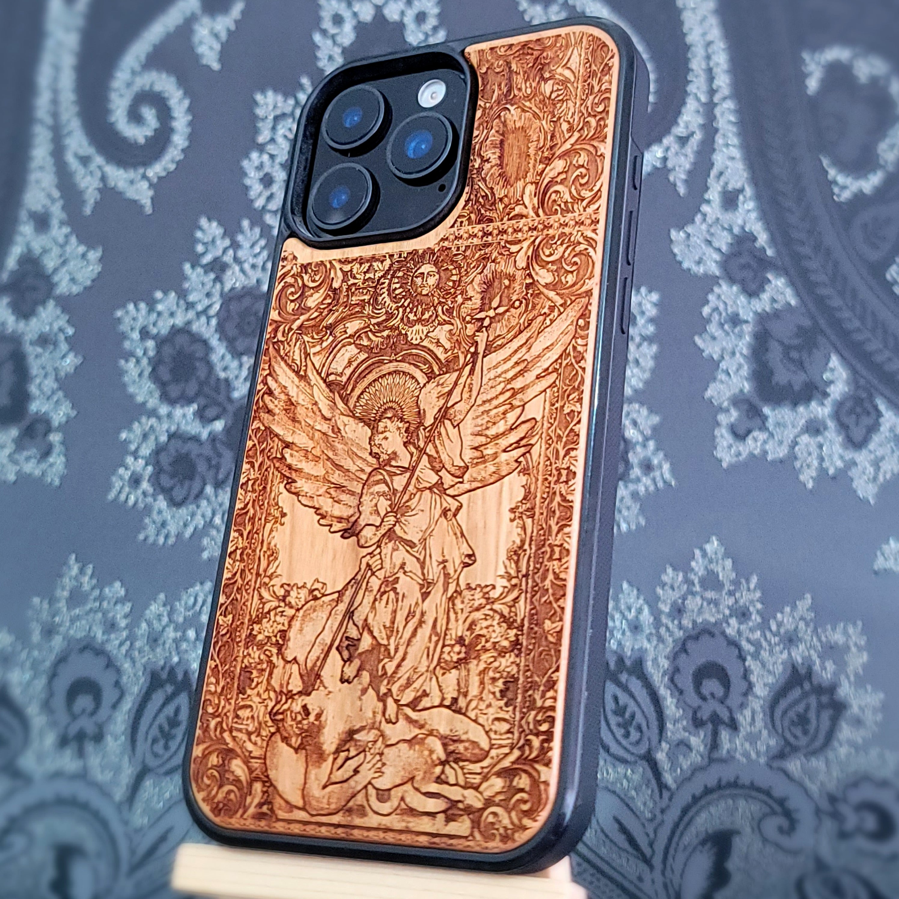 Deep laser engraved wooden phone case featuring Saint Michael Archangel fighting a demon with detailed religious artwork on natural wood for iPhone and Samsung Galaxy models.