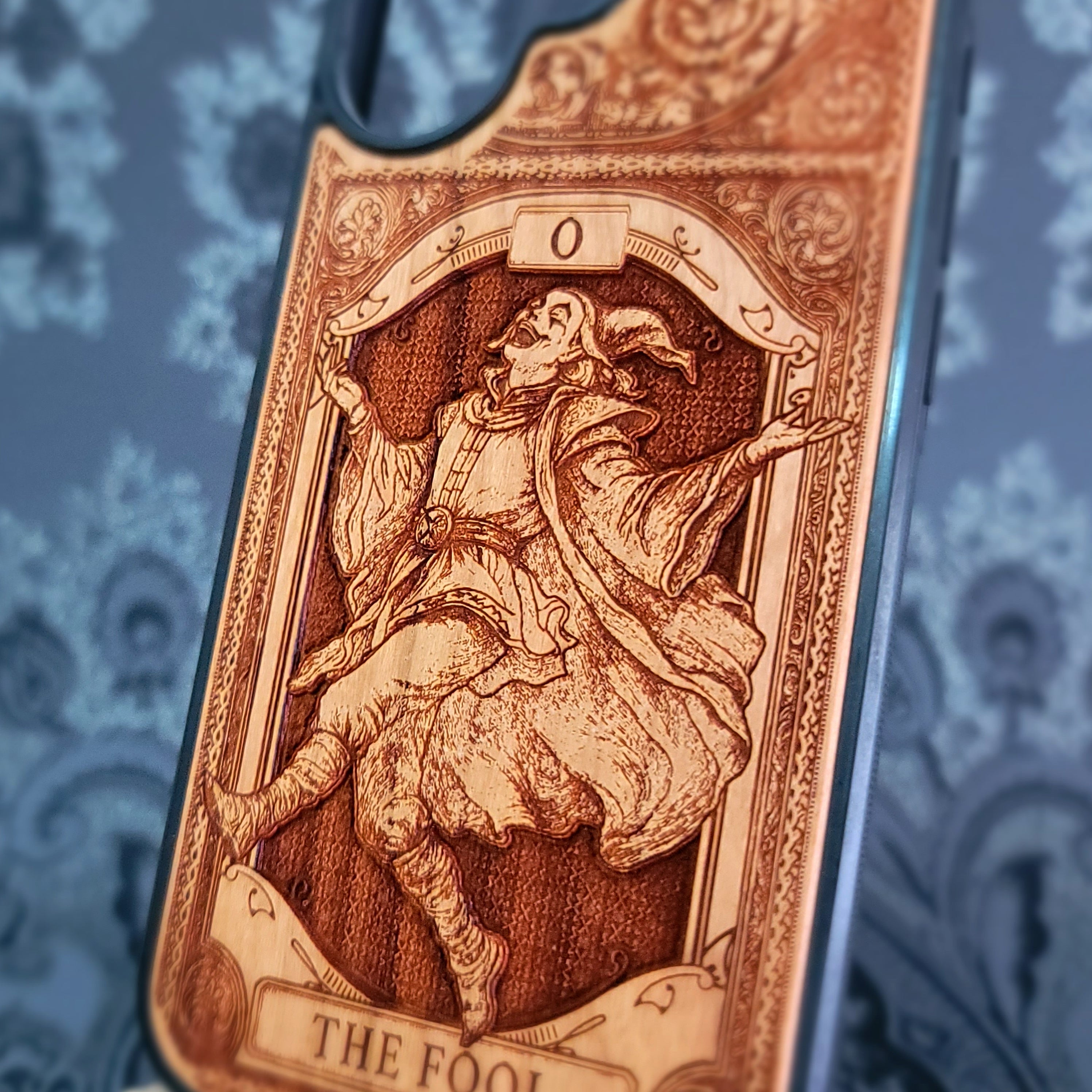 Deep laser engraved wooden phone case featuring The Fool tarot card with mystical celestial details on natural wood for iPhone and Samsung Galaxy models.