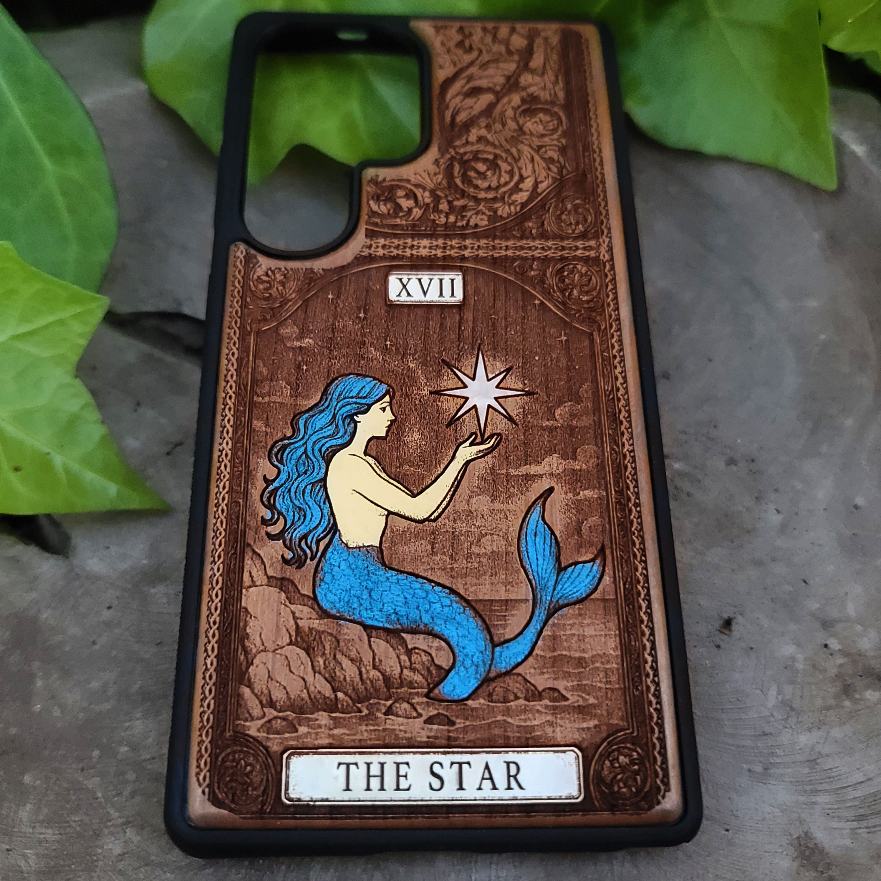 Phone case with mermaid design and 'The Star' tarot card symbolism on a wooden background.