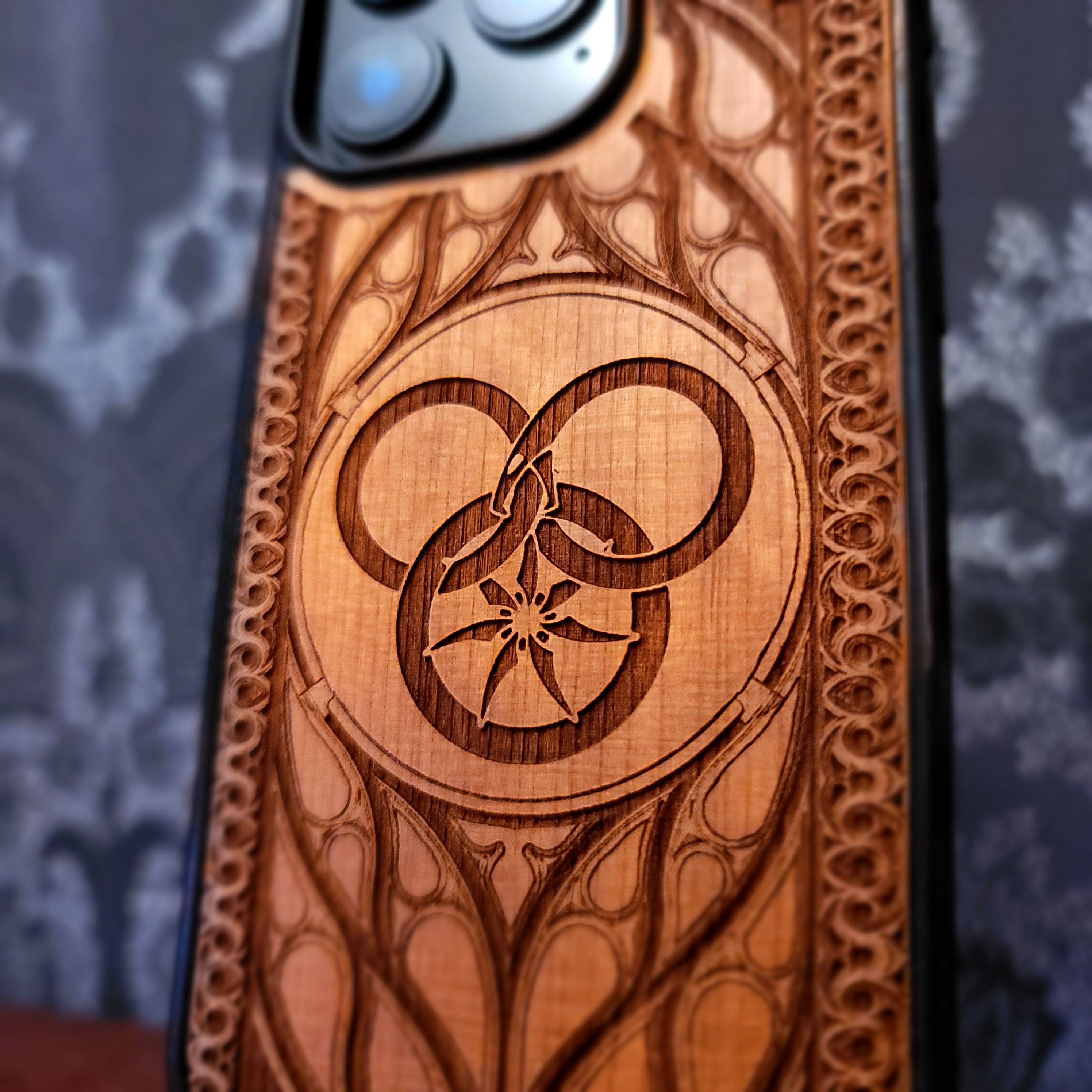 Deep laser engraved wooden phone case featuring a Wheel of Time inspired fantasy symbol on natural wood for iPhone and Samsung Galaxy models.