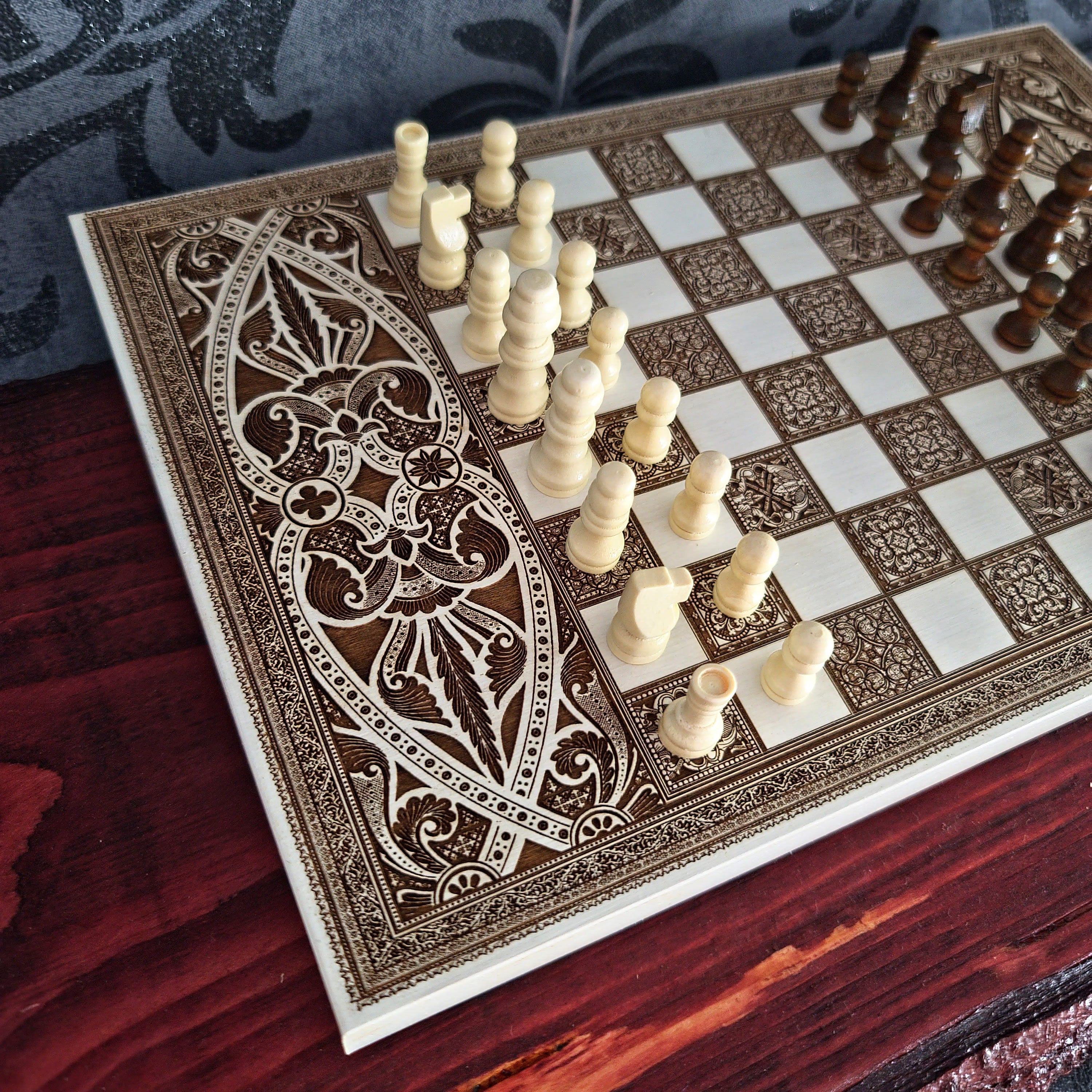 An ornate rectangular chessboard with intricate brown and cream patterns, set on a dark wooden table with chess pieces arranged on it.