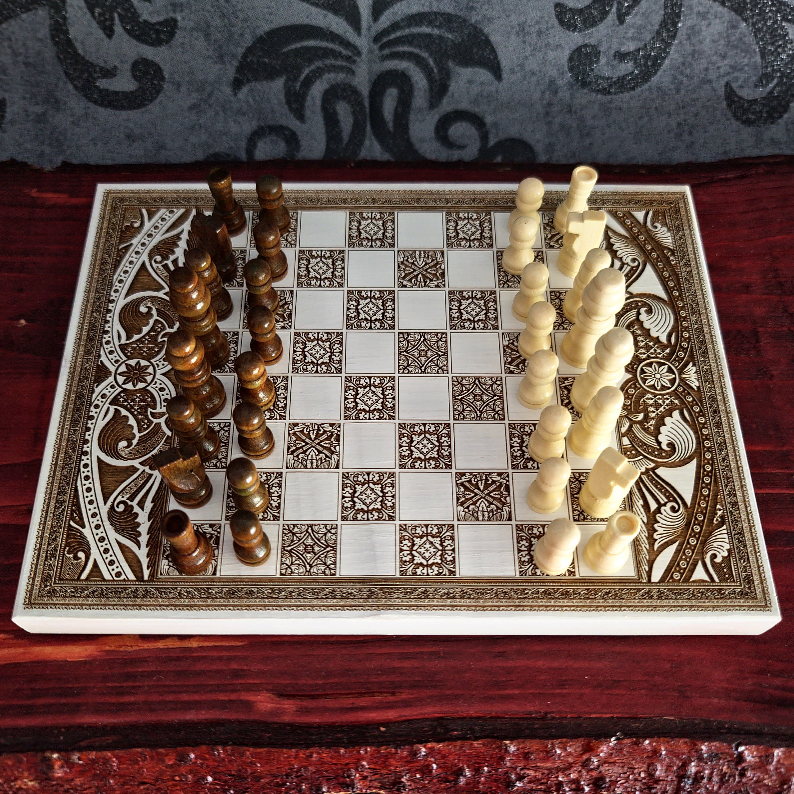 An ornate rectangular chessboard with carved decorative borders, shown with wooden and ivory chess pieces arranged