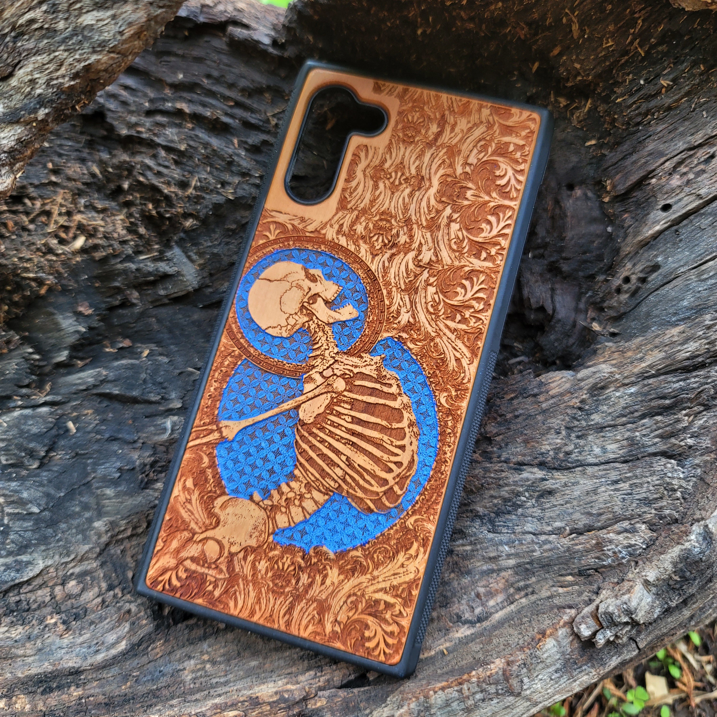 Close-up of handcrafted cherry wood phone case with detailed skeleton engraving and Gothic blue accents.
