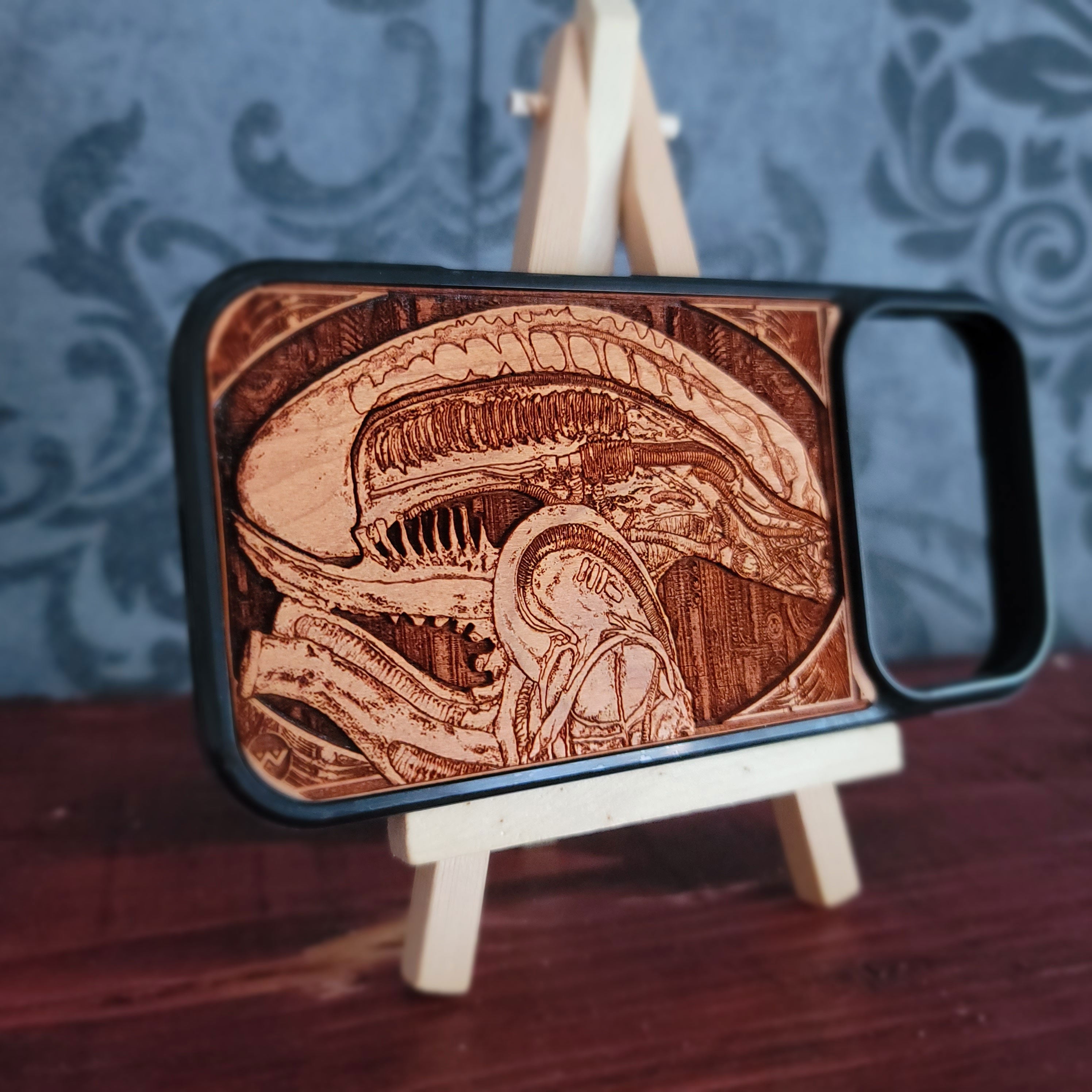 A wooden phone case with a detailed laser-engraved Alien Xenomorph design