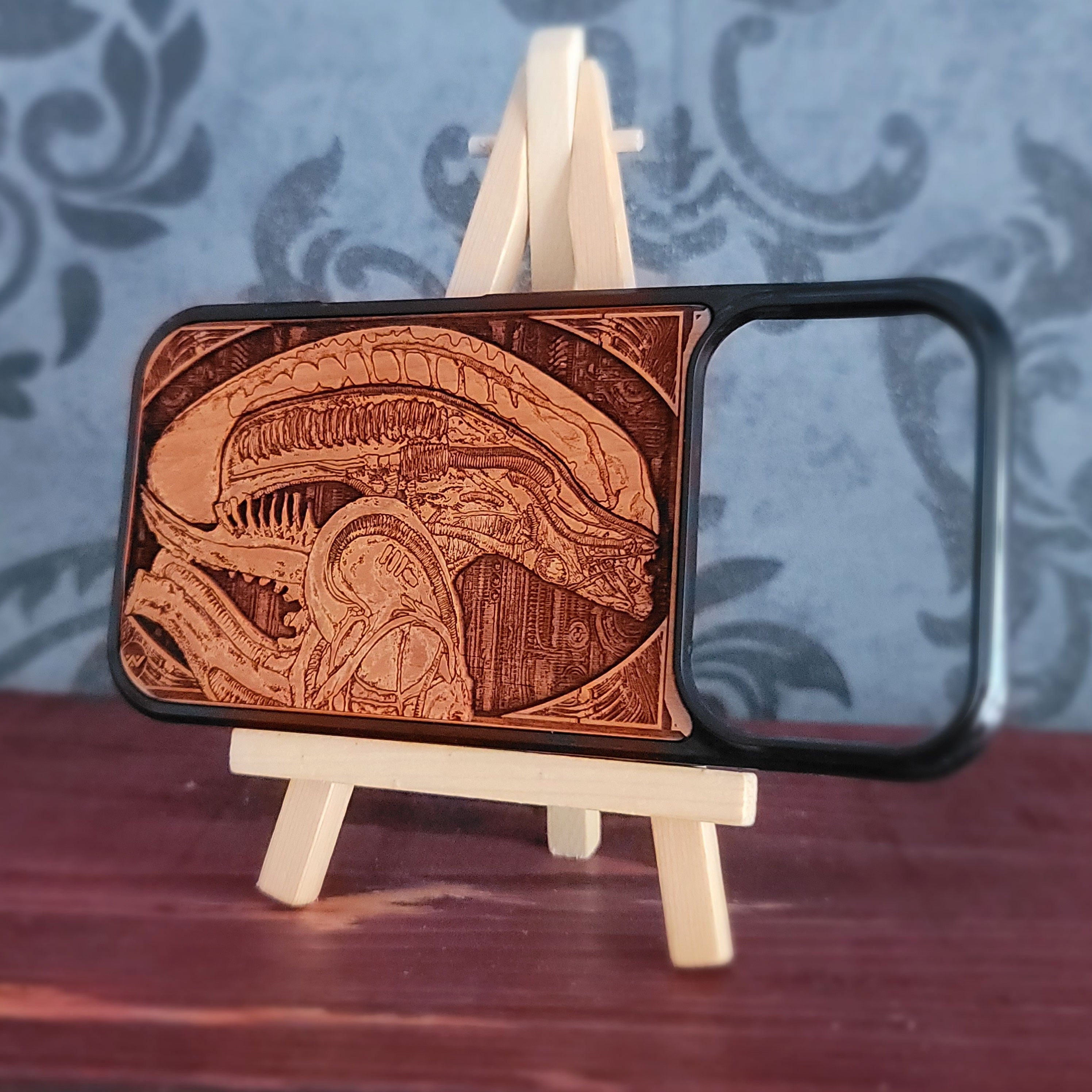 A wooden phone case with a detailed laser-engraved Alien Xenomorph design