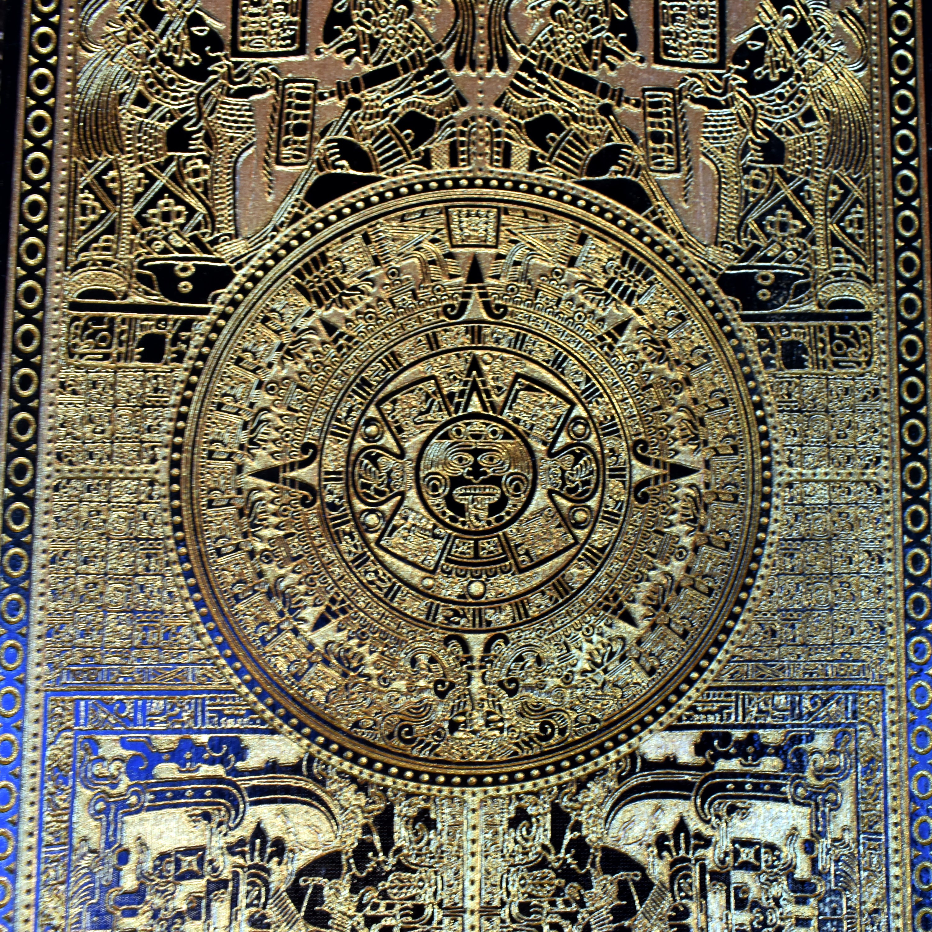 Engraved Aztec sunstone symbol on dark wood, Mayan calendar style decor.