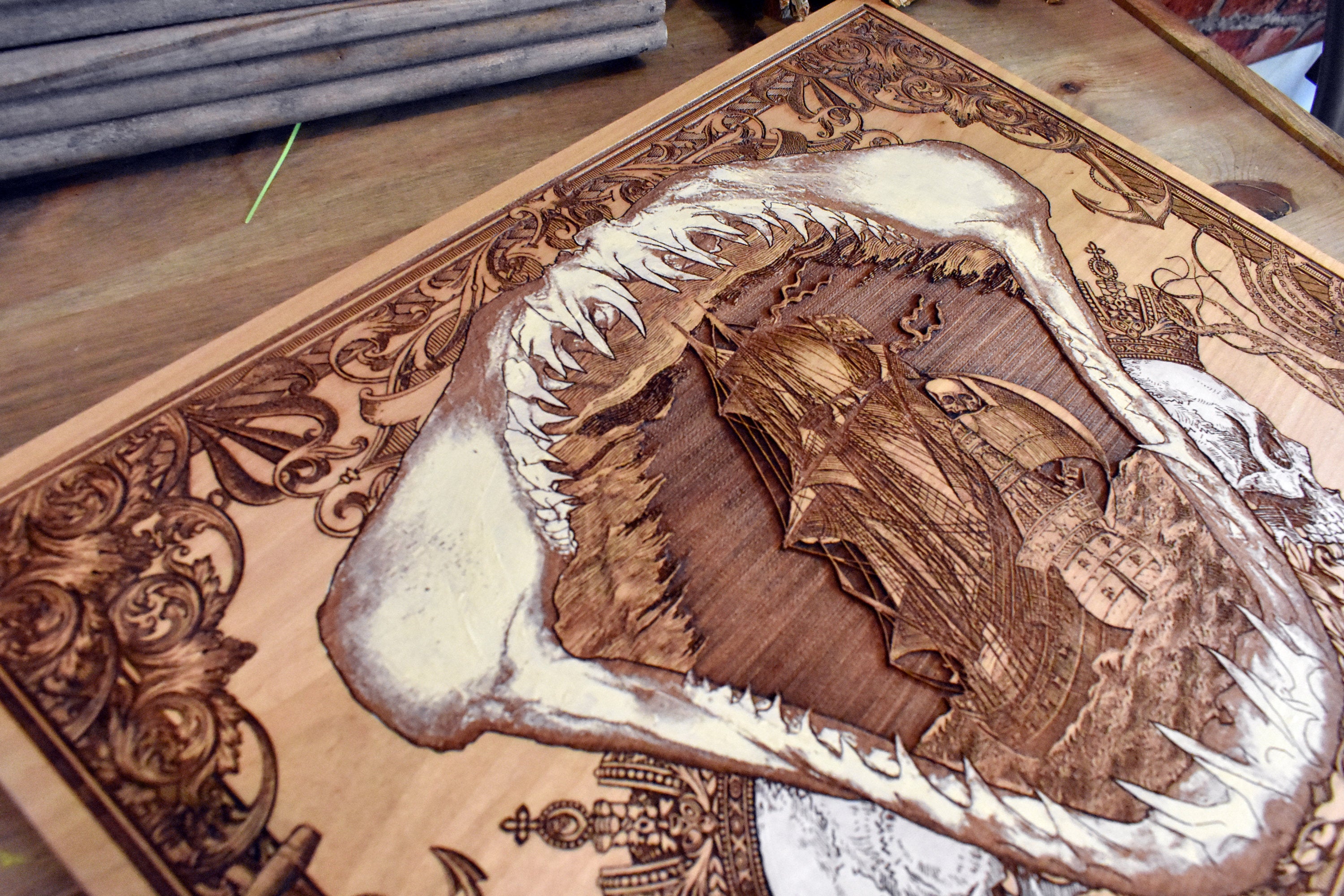 Wooden wall decor of pirate ship trapped in shark jaw, maritime style.