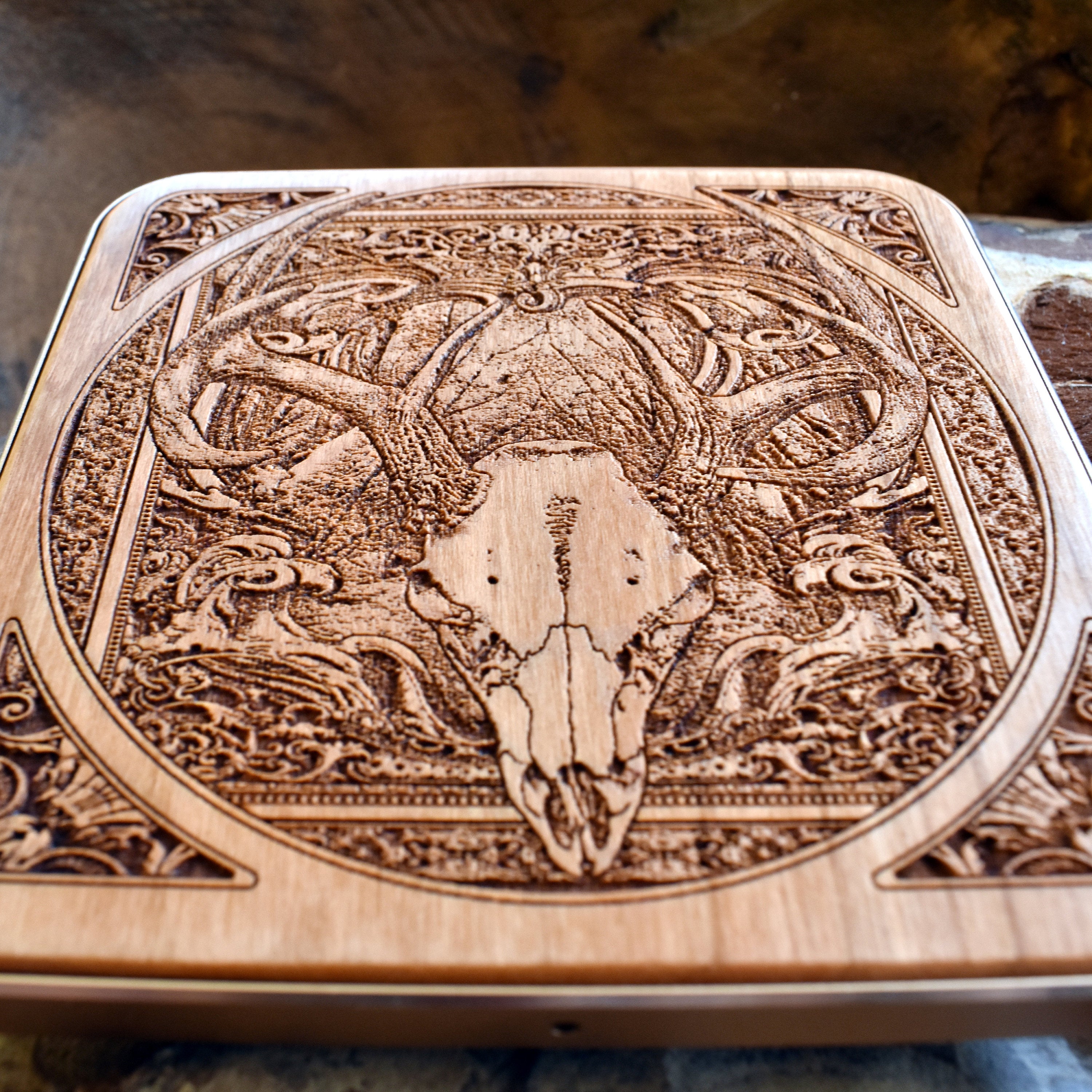 Wooden charging pad with engraved deer skull design styled on a minimalist desk.