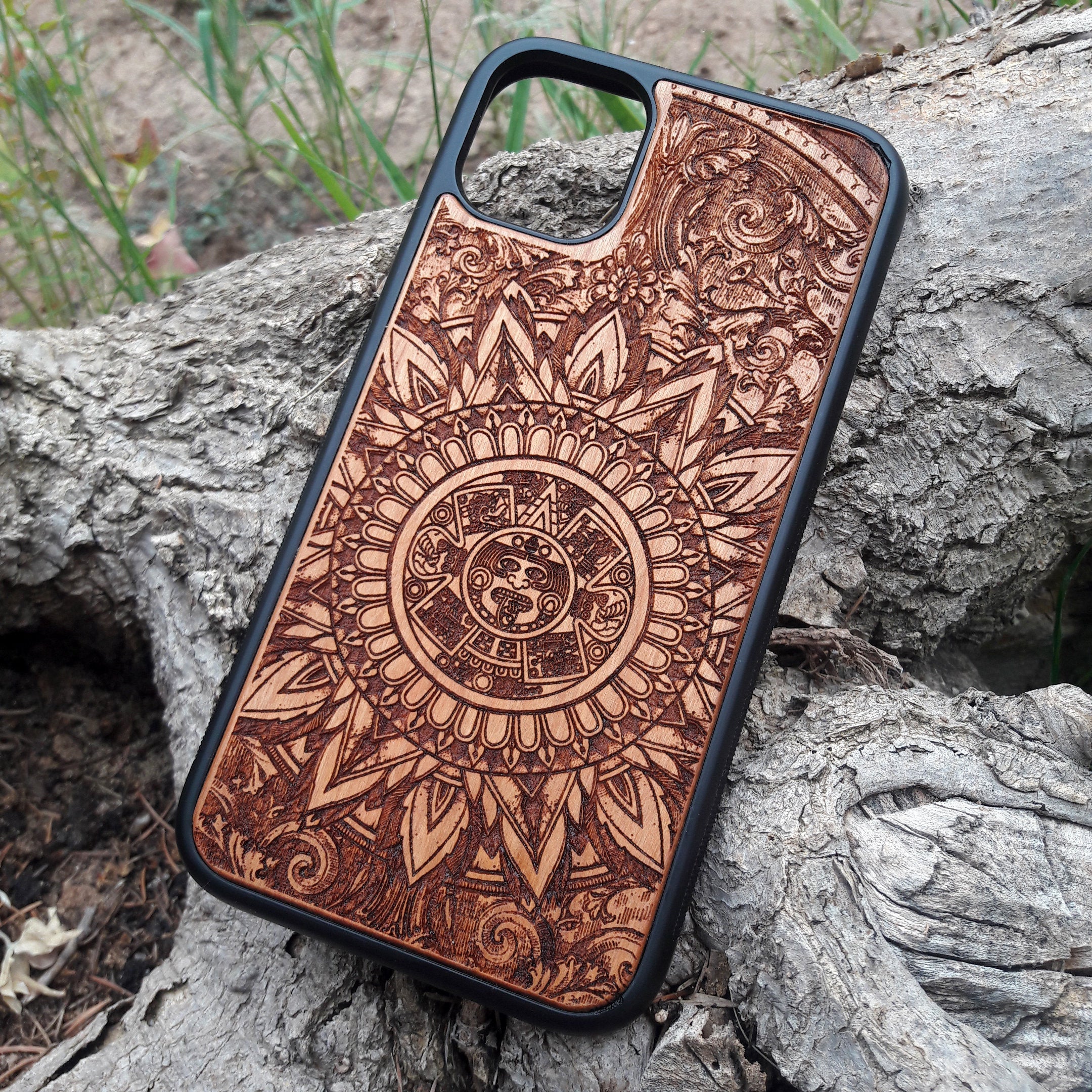 Intricately engraved wooden phone case featuring an Aztec calendar design with ornate details, crafted for durability and style. Compatible with iPhone and Samsung Galaxy S models, this case combines cultural artistry with premium protection for your device.