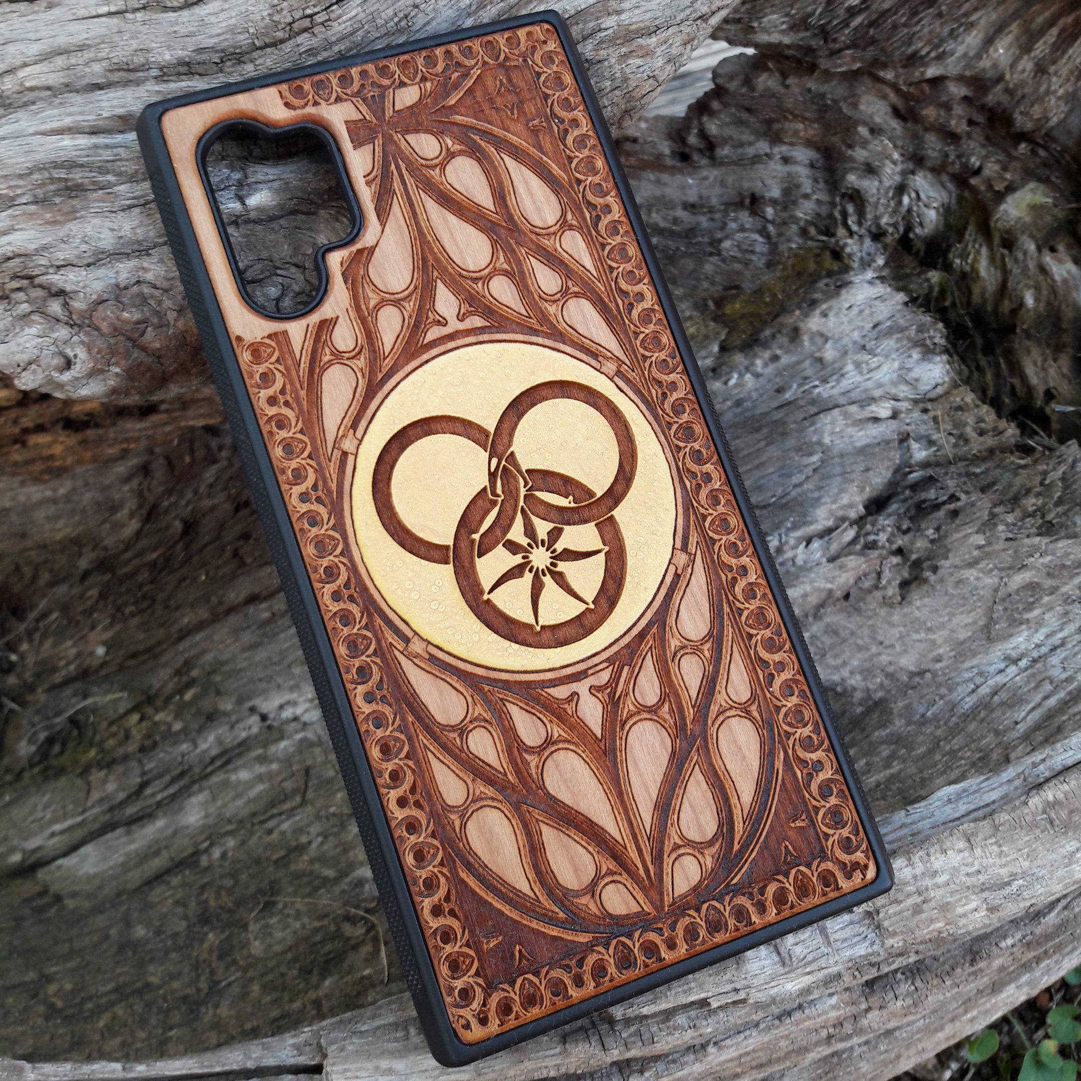 Wooden phone case featuring a detailed Wheel of Time-inspired design, showcasing intricate engravings of the Aes Sedai symbol and runes. The laser-engraved design captures the essence of Robert Jordan's iconic fantasy series. Compatible with iPhone , 15, 14, 13, 12, 11 Pro Max Mini, and Samsung Galaxy S, S24, S23, S22, S21, S20 Ultra, Plus, Note 20. A perfect, durable accessory for fans of the Wheel of Time series, blending art and protection.
