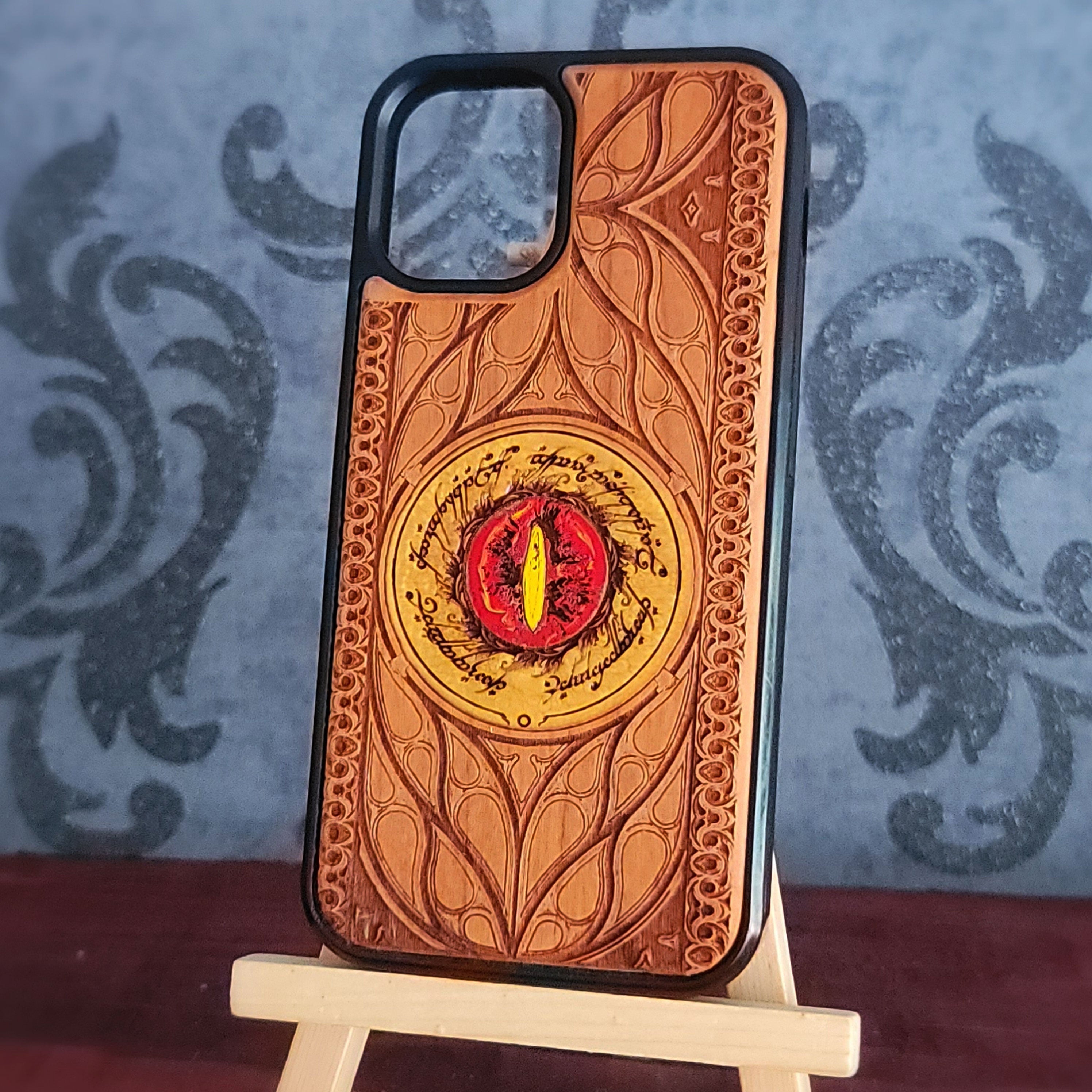 A phone case with an embossed Hobbit door design featuring a red and yellow eye of Sauron in the center, displayed on a small wooden stand.