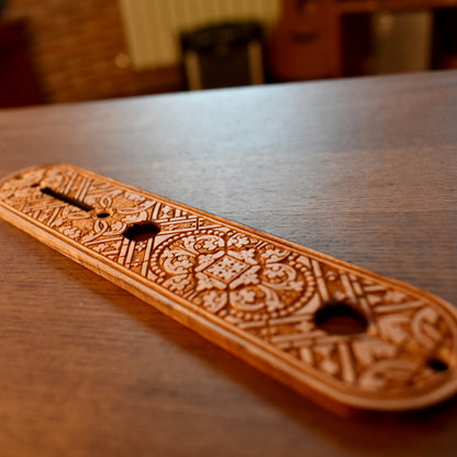Laser‑engraved medieval pattern on wood truss rod cover for guitar — intricate Gothic‑style motif, warm brown finish.