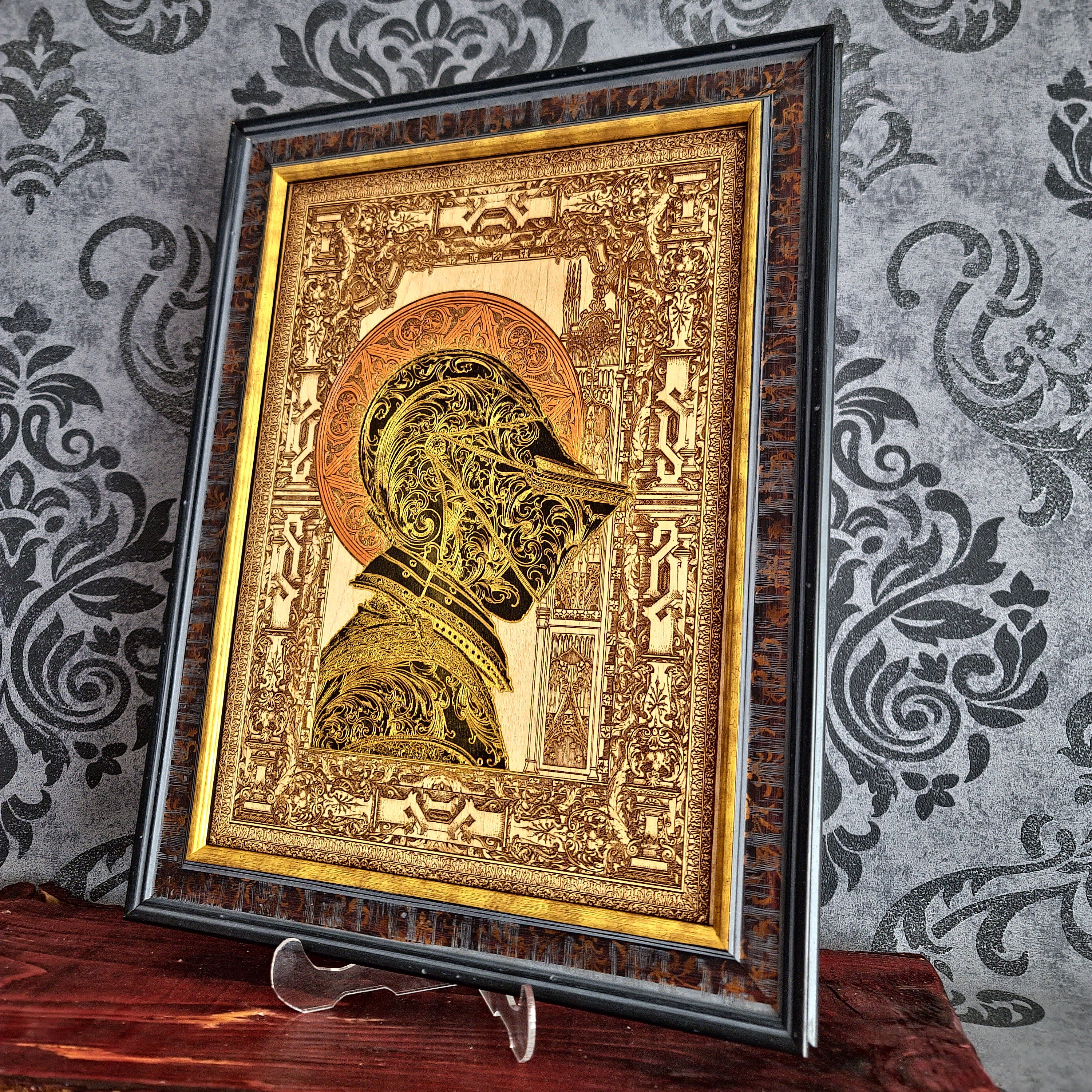 Black-and-gold medieval knight helmet maple wood wall art, angled view in a wide gold-leaf frame