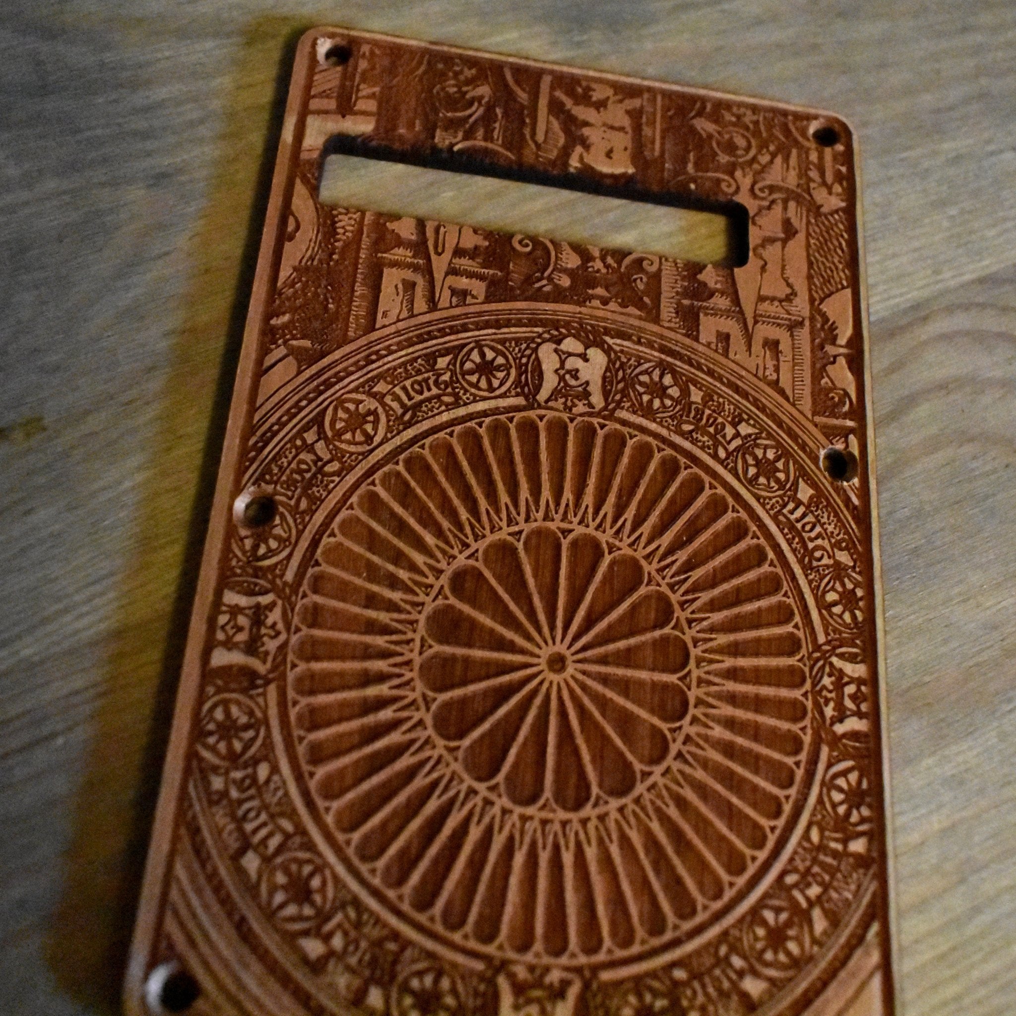 Close-up of intricate Gothic engraving on handcrafted cherry wood tremolo cover for Fender Stratocaster guitar.