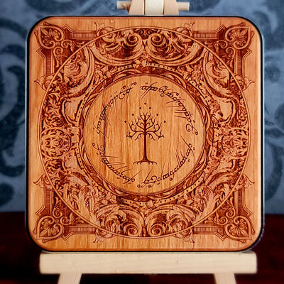 A square wooden wireless charger with rounded corners, featuring an intricate laser-engraved design inspired by 'The Lord of the Rings' with the Tree of Gondor in the center and the Ringwraith inscription around it. 