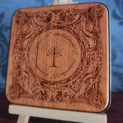 A square wooden wireless charger with rounded corners, featuring an intricate laser-engraved design inspired by 'The Lord of the Rings' with the Tree of Gondor in the center and the Ringwraith inscription around it. 
