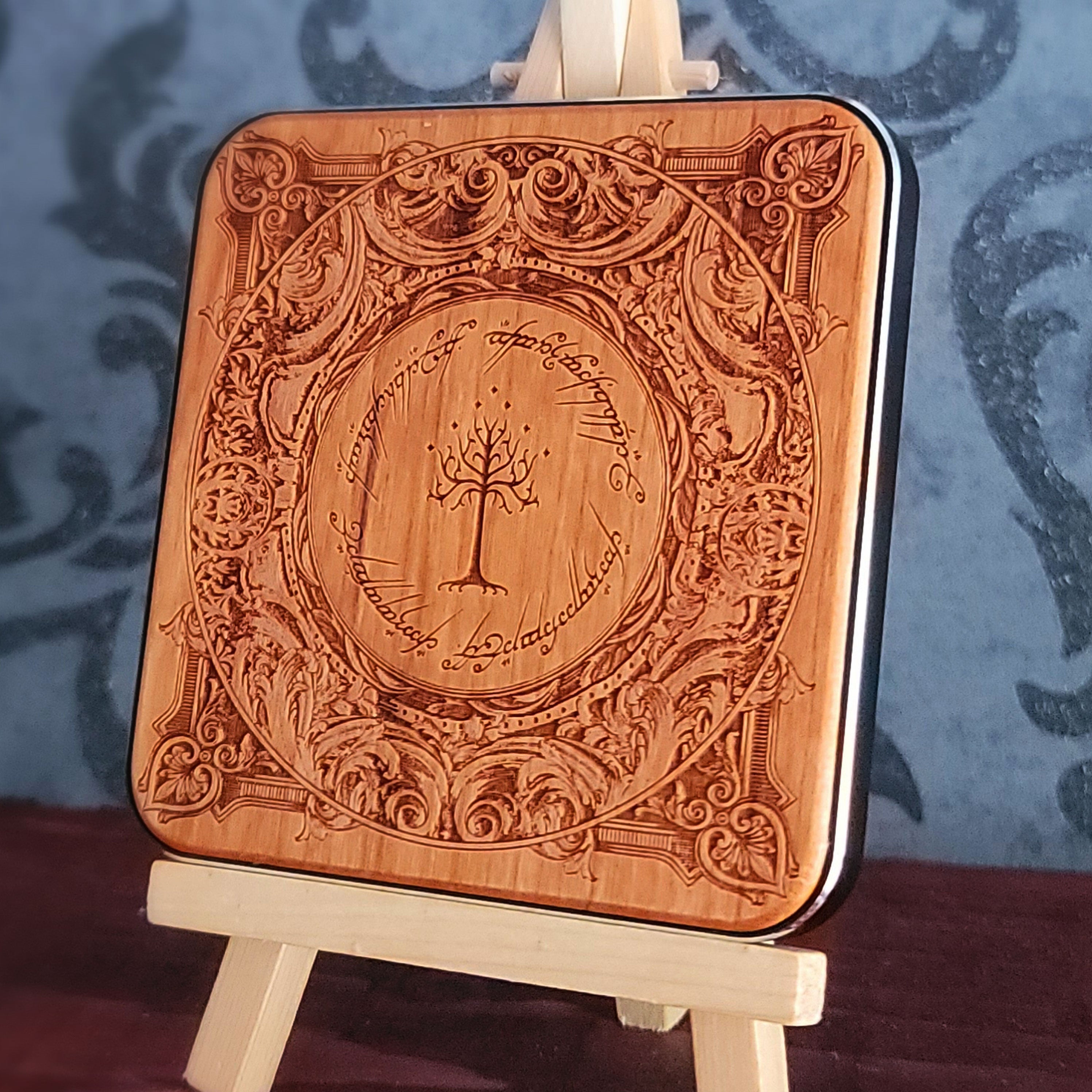 A square wooden wireless charger with rounded corners, featuring an intricate laser-engraved design inspired by 'The Lord of the Rings' with the Tree of Gondor in the center and the Ringwraith inscription around it. 
