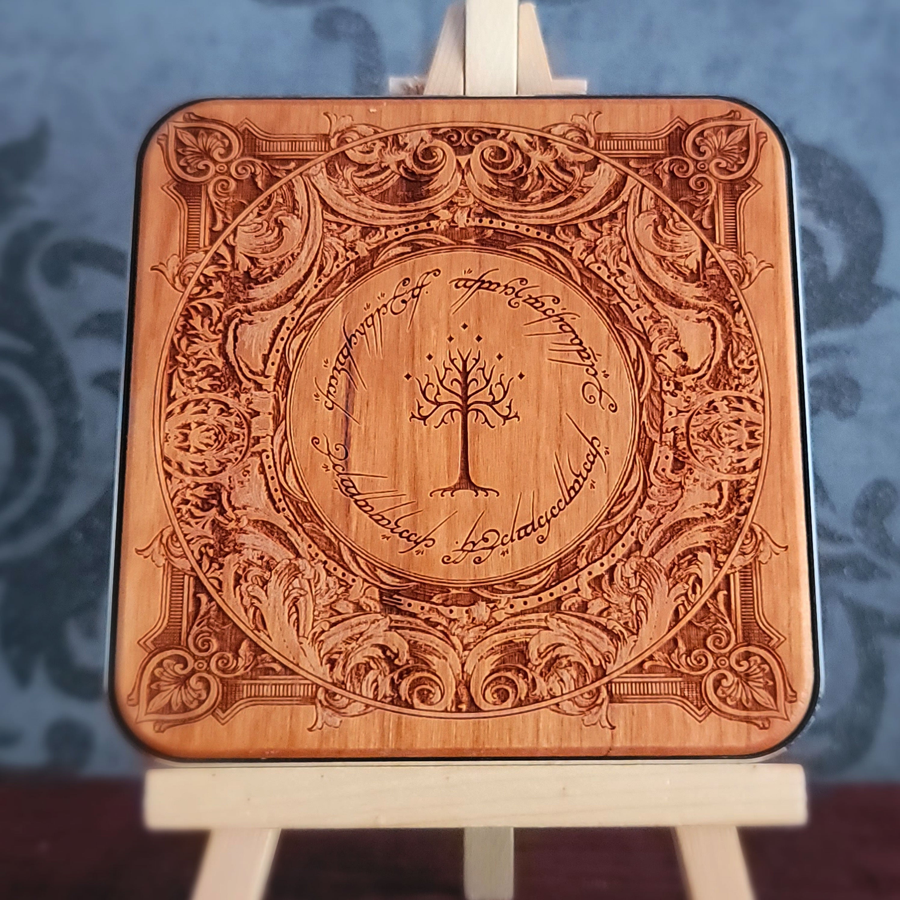 A square wooden wireless charger with rounded corners, featuring an intricate laser-engraved design inspired by 'The Lord of the Rings' with the Tree of Gondor in the center and the Ringwraith inscription around it. 