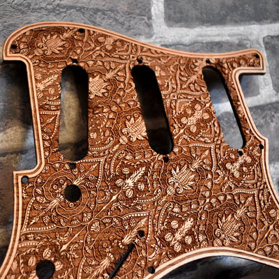 Close-up of laser-engraved cherry wood pickguard for Fender Stratocaster, showcasing intricate artwork