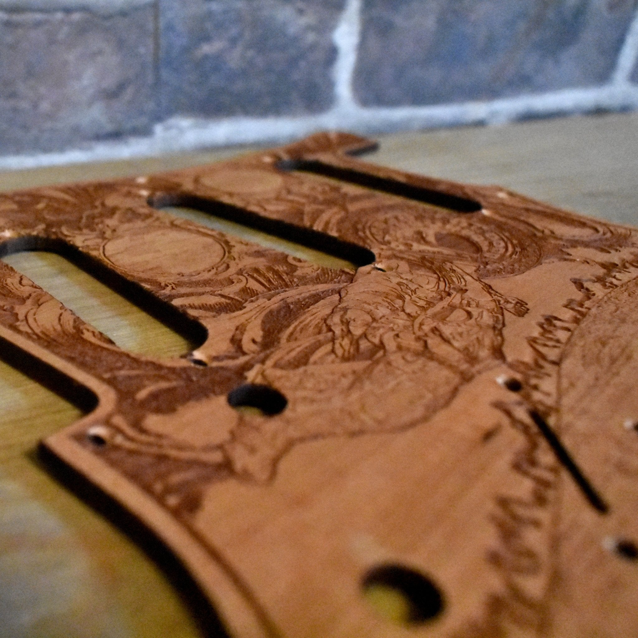 Close-up of laser-engraved cherry wood guitar pickguard with detailed artwork.