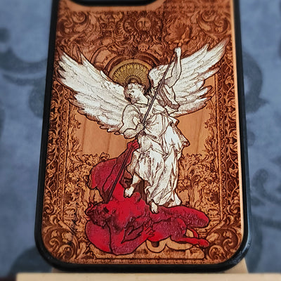 A close-up of a phone case featuring a detailed religious illustration of Saint Michael angel with large white wings standing on a red creature, set against an ornate brown baroque-style background.