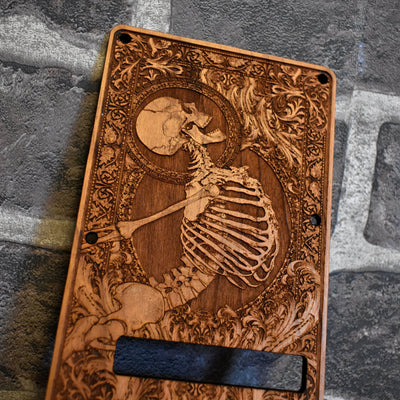 Close-up of laser-engraved skeleton artwork on cherry wood tremolo cover for Strat