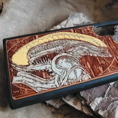 Alien-inspired gothic artwork engraved on a wooden phone case, compatible with iPhone and Samsung Galaxy