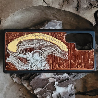 Alien-inspired gothic artwork engraved on a wooden phone case, compatible with iPhone and Samsung Galaxy